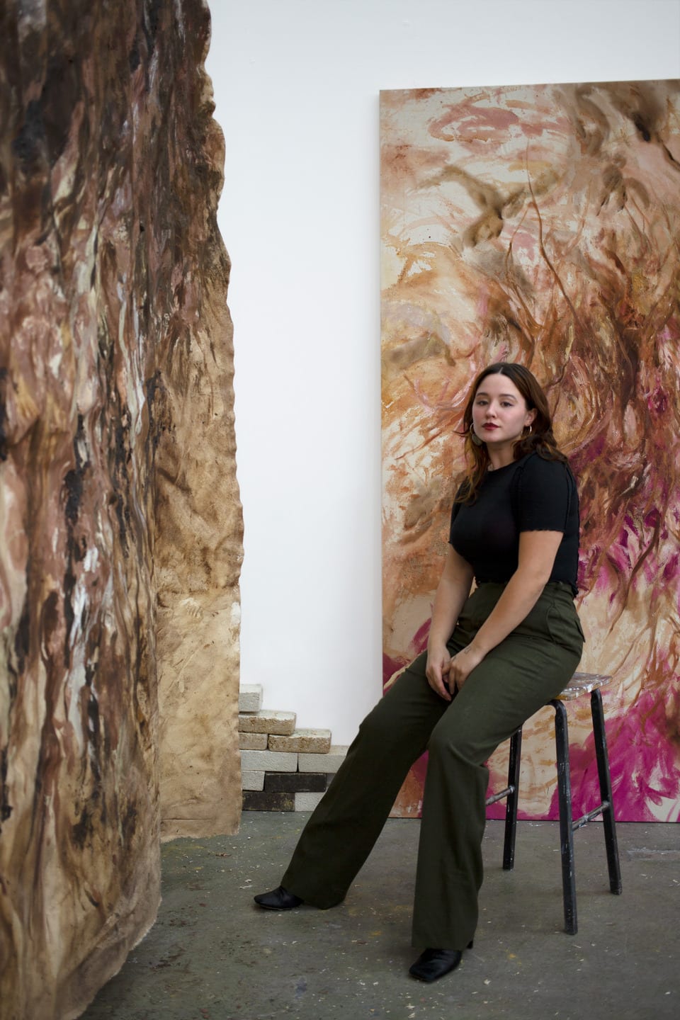 Julia Bennett sitting on a stool in front of her paintings in the studio