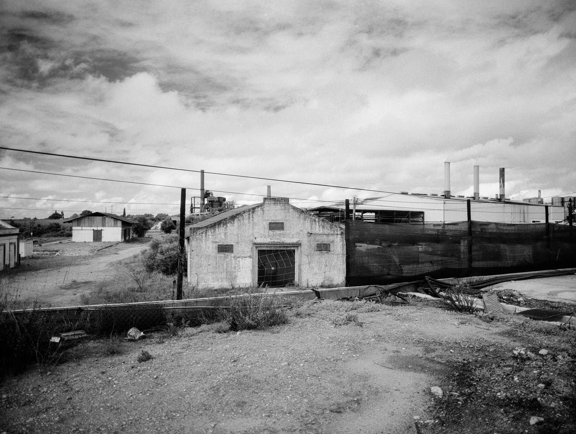 Abandoned industrial complex with olive bagasse incinerated plant emitting smoke in background. Tile in shrub lower left frame.