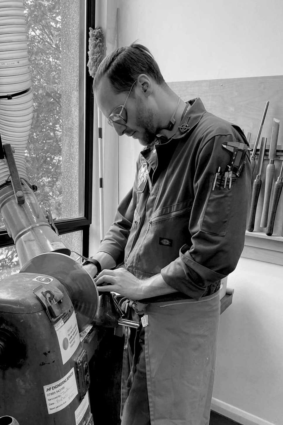 Designer Britton Kroessler working on a wood lathe wearing a sick jumpsuit covered in heavy metal patches.