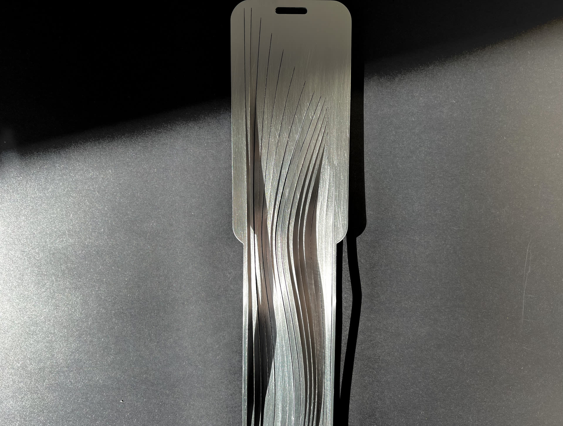 Steel smartphone shaped object which continues beyond the bottom of the phone in strips suggesting that the object is endless. 