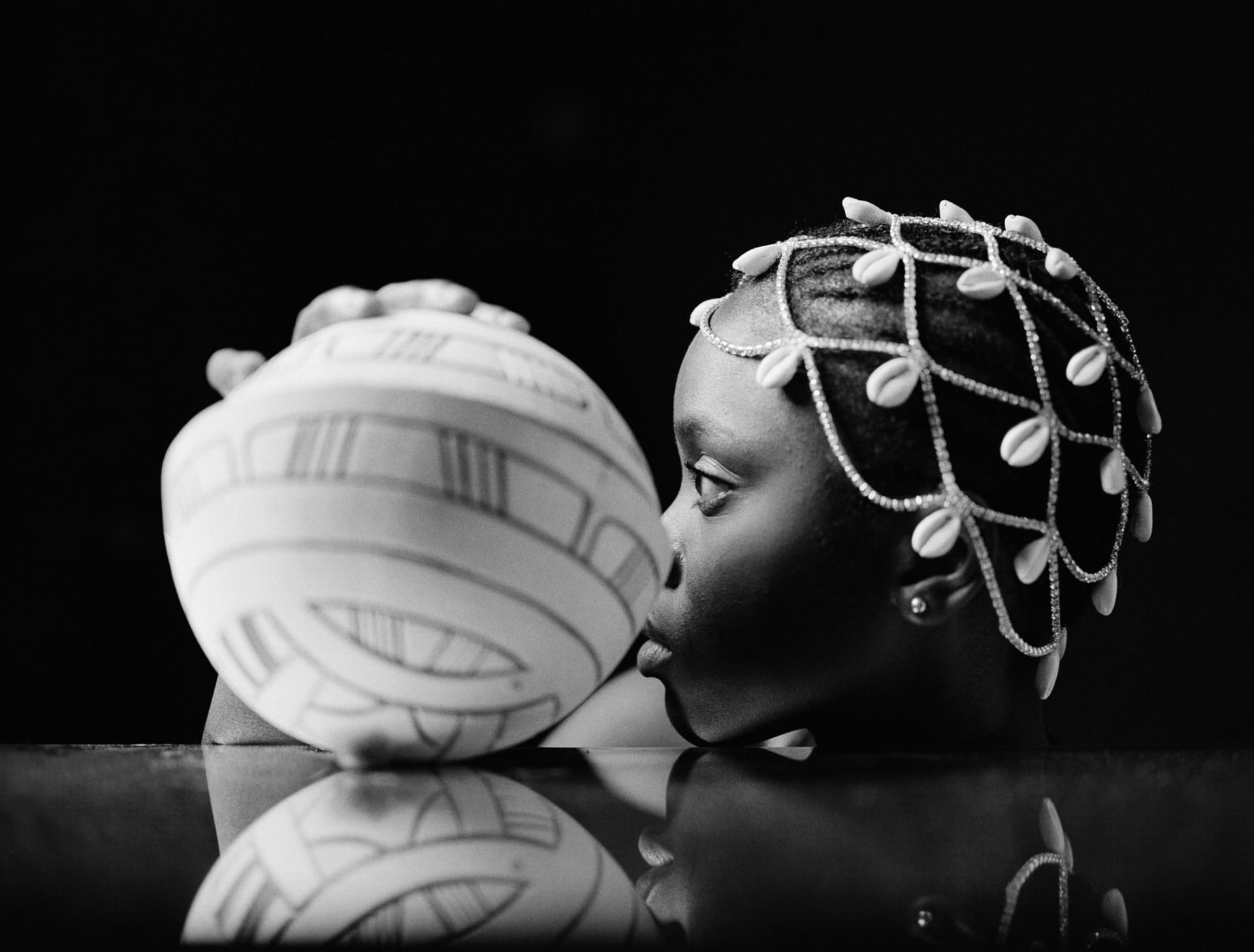 side profile image of black girl holding a calabash on a mirror looking to the front. 