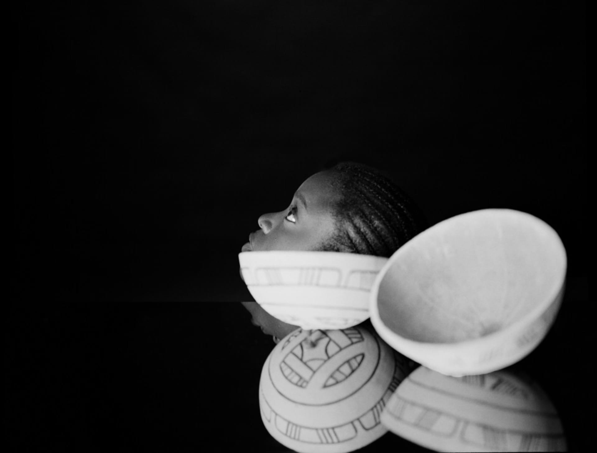 B & W  portrait image of a girl on top of a mirror and a calabash. She is looking up.