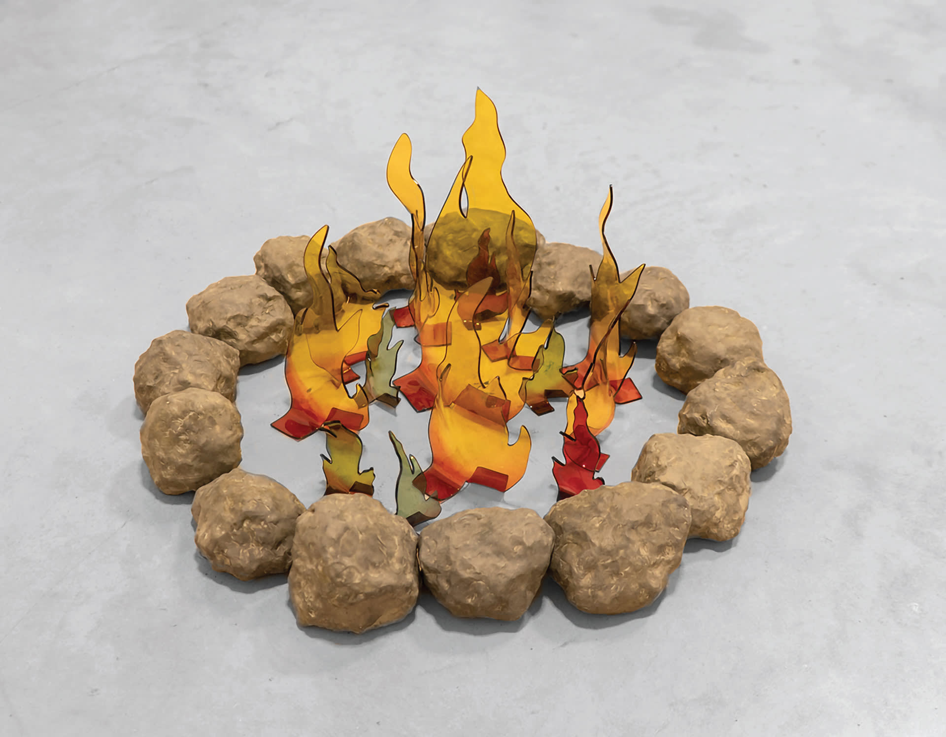 A fire pit made with grey clay stones surrounding red, yellow, green and blue flames in acrylic glass