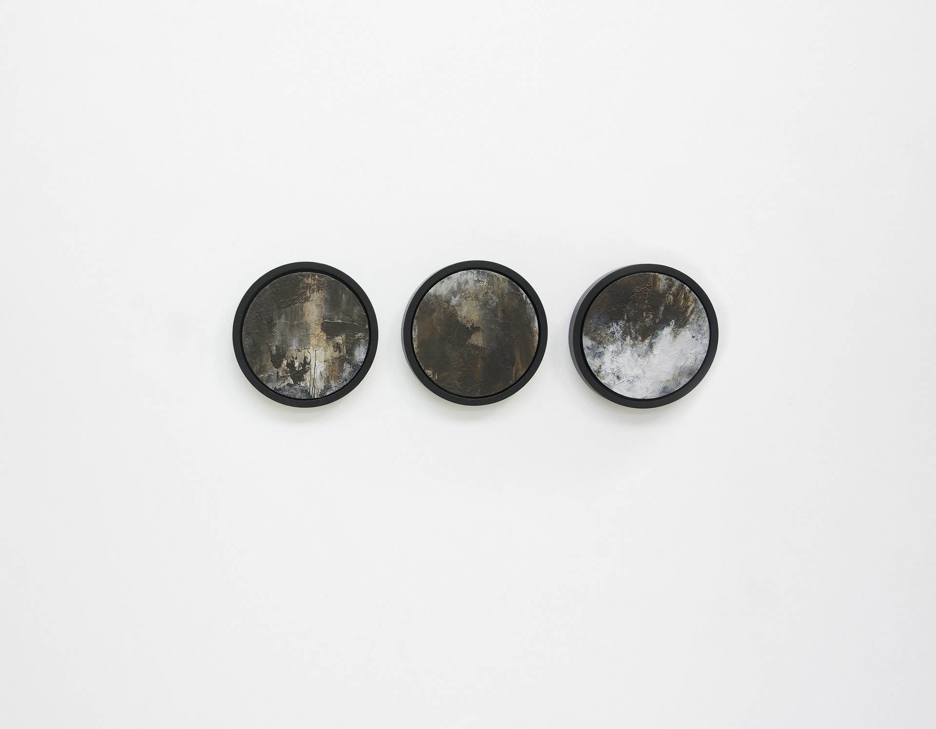 Three circular abstract wood panel canvases hang on a white wall. They are in black frames.