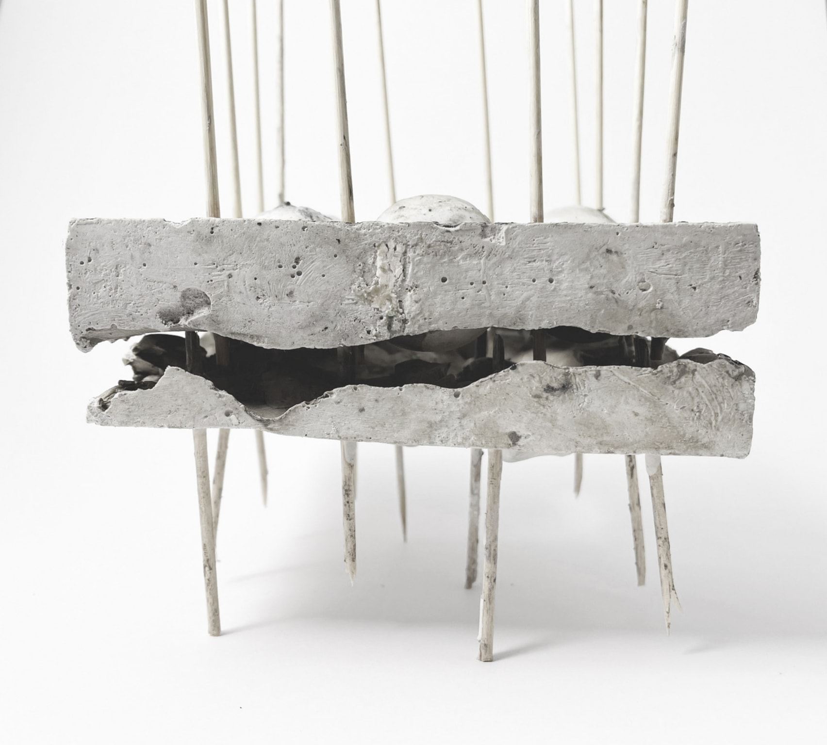 Concept model, sticks passing vertically through concrete block with crack through centre. 