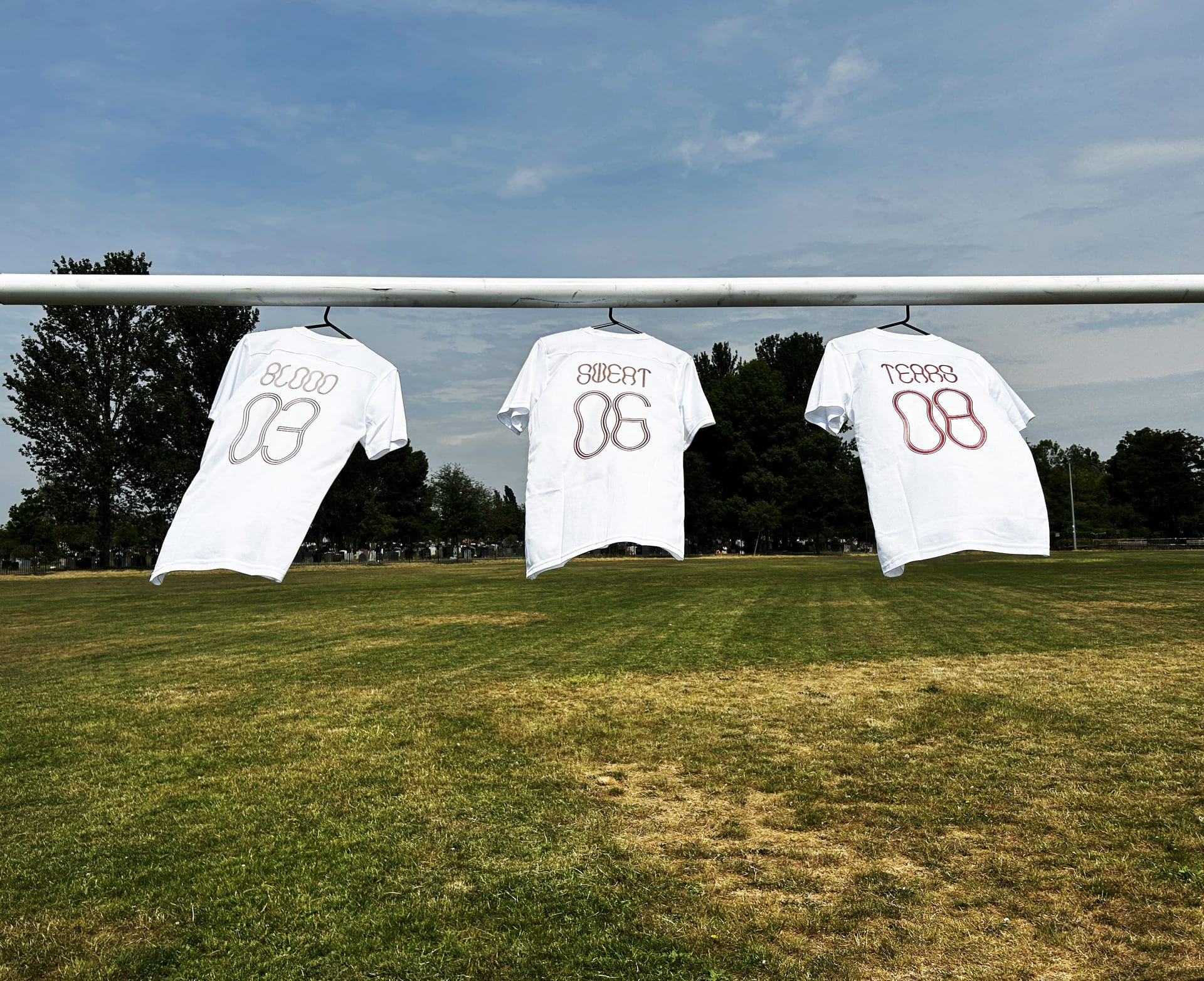 3 white football shirts hanging on goal posts. The first shirt says blood, the second says sweat and the third says tears.