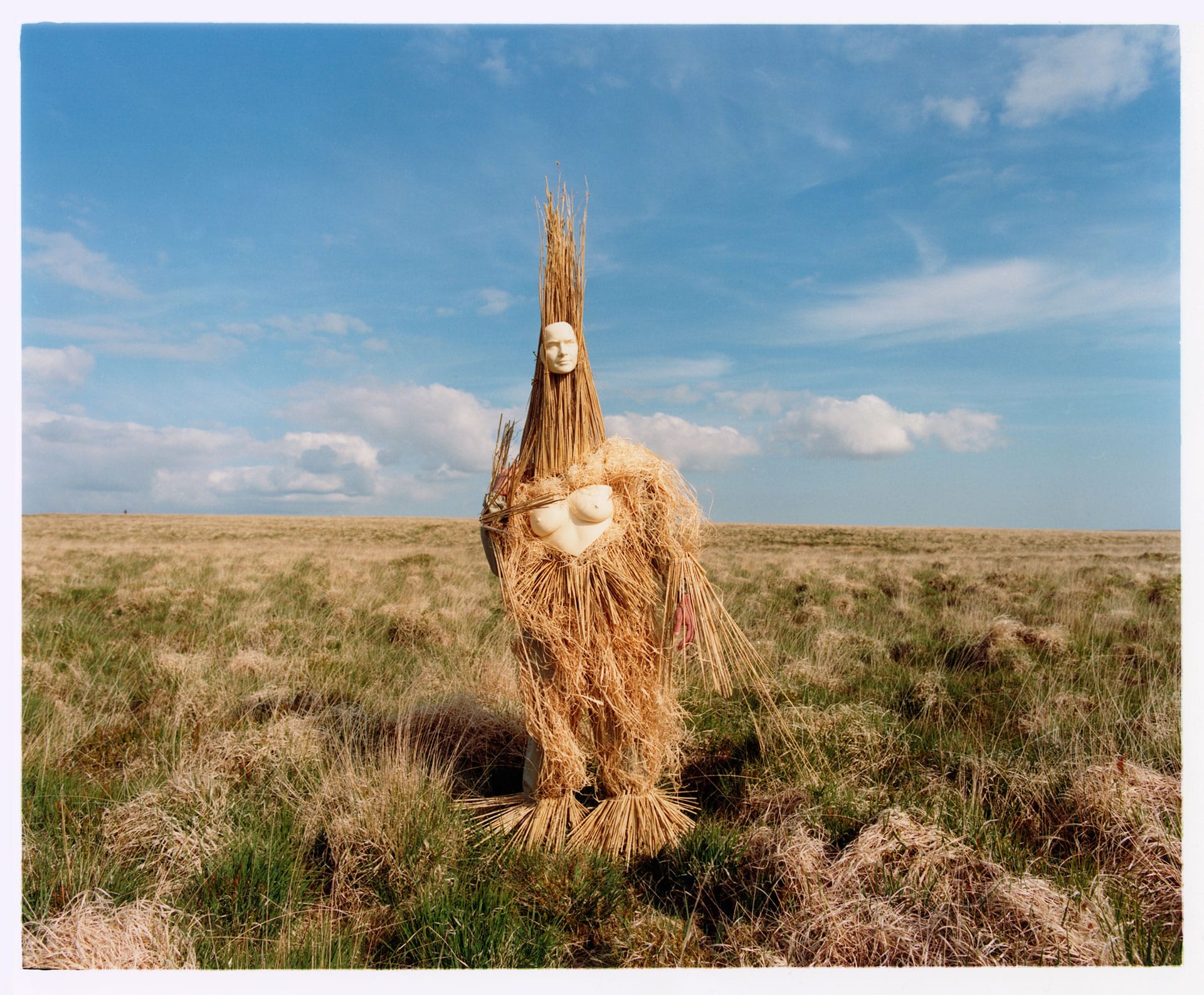 A lone figure of straw and masquerade standing in a rural landscape
