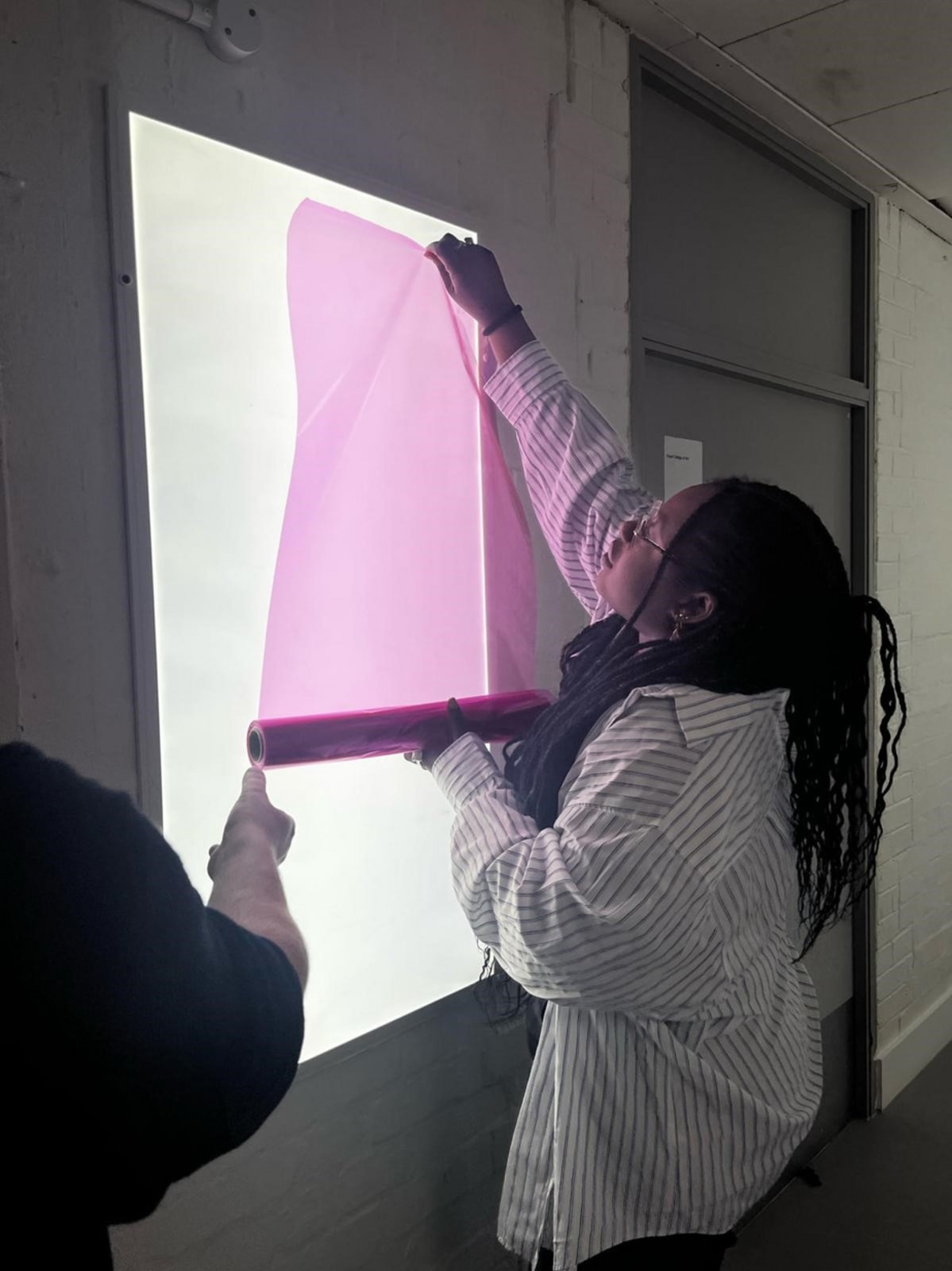 Oyinkan doing colour tests with pink film over a light box for the hallway intervention in her Across RCA project.  