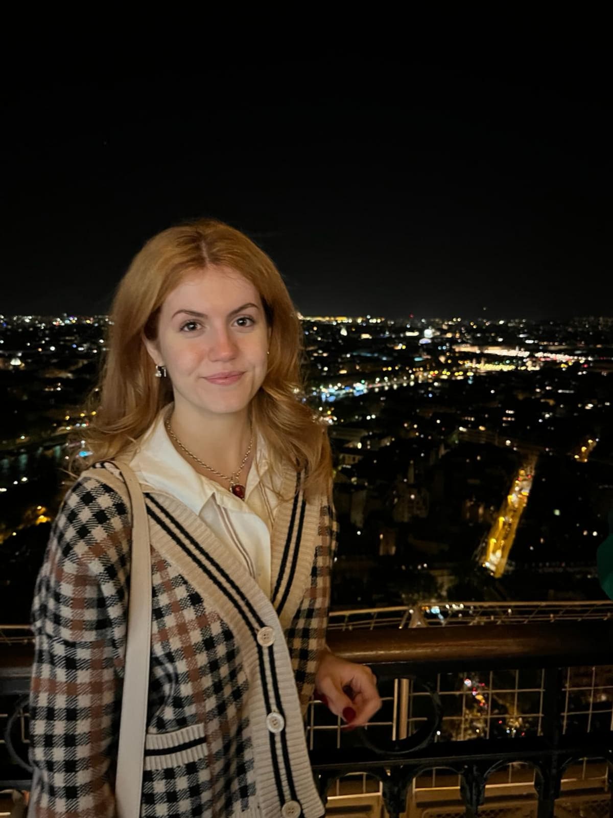 Elis stands before balcony railings, facing the camera. Dark cityscape in the background.