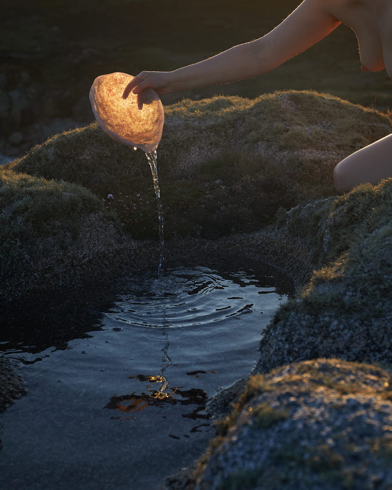 Water splashes at twilight, poured between clifftop rock pools. 