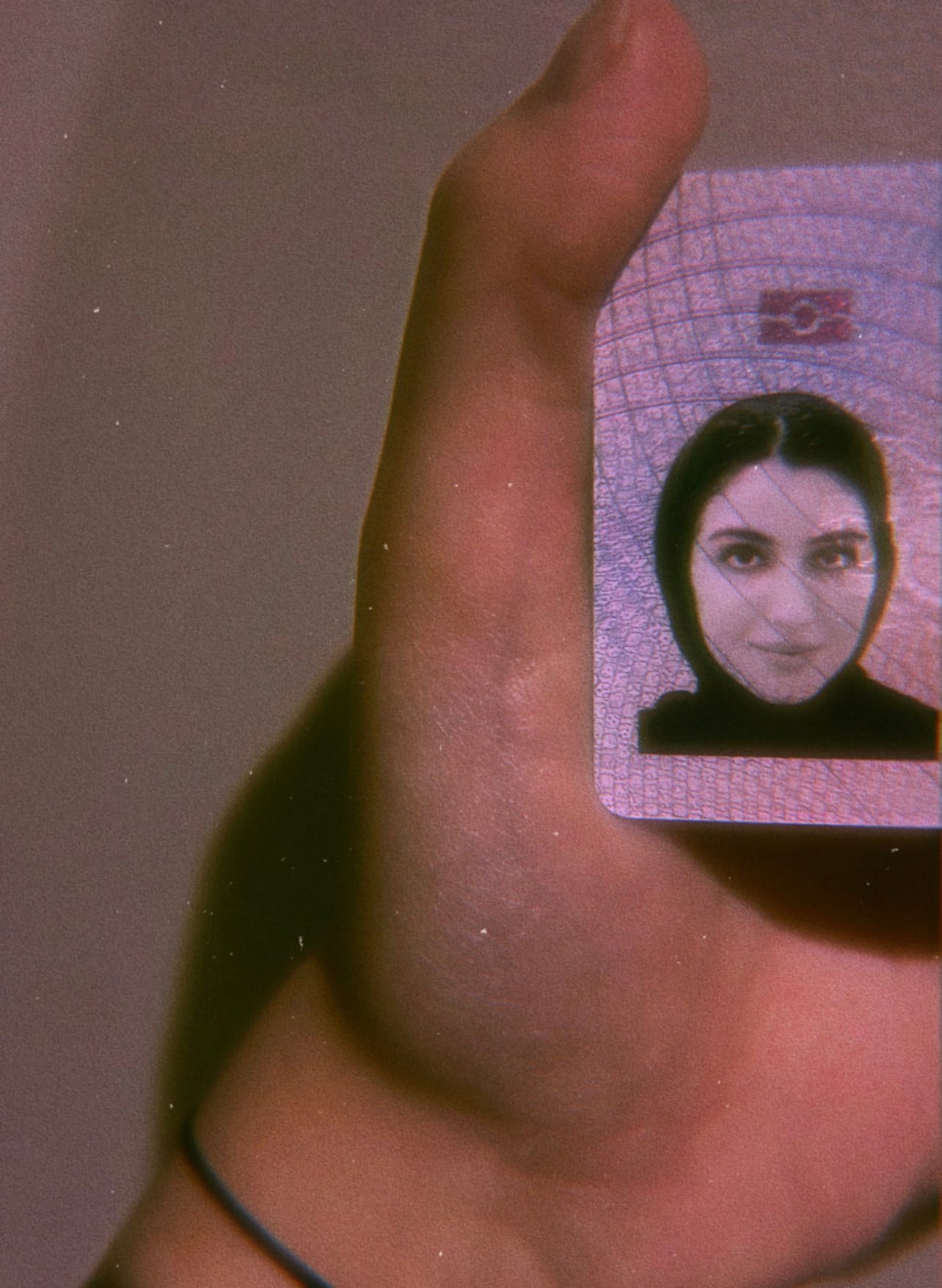 A hand holding up a residency permit. The image is cropped so only the ID photo, depicting a woman in a headscarf, is showing.