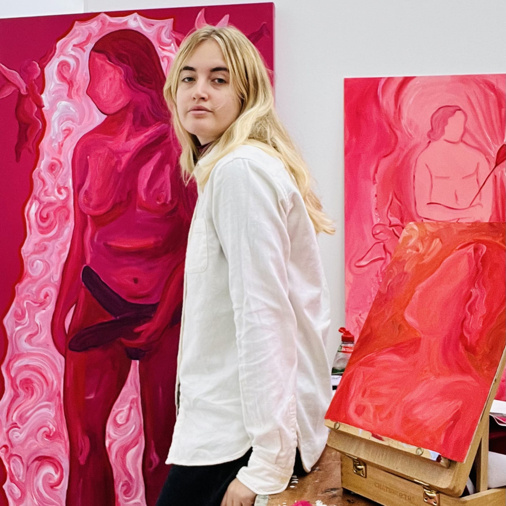 Louise Benton, female artist, standing before a selection of pink paintings in her studio. 