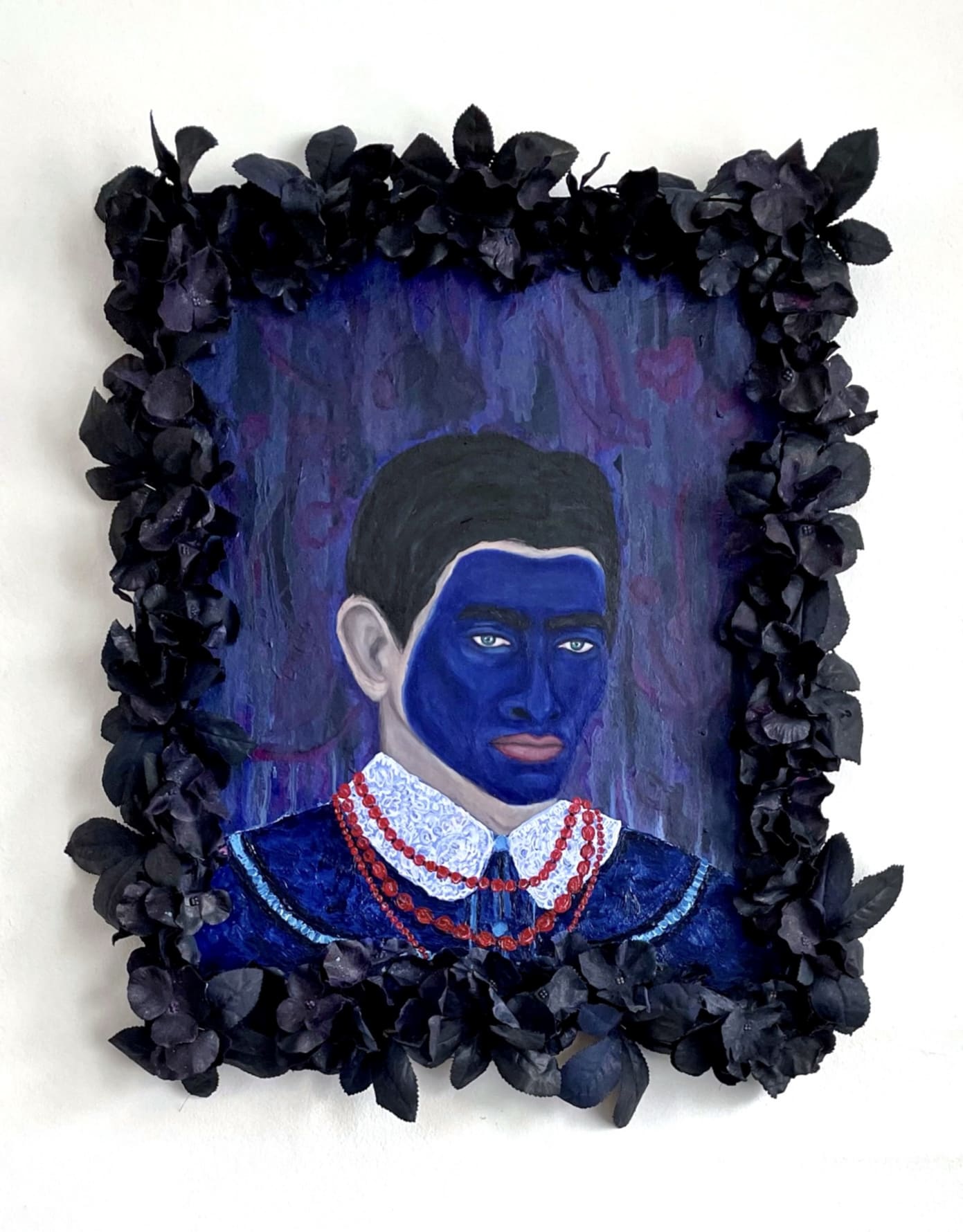 male figure with blue painted face and red necklace with flowers attached onto the frame