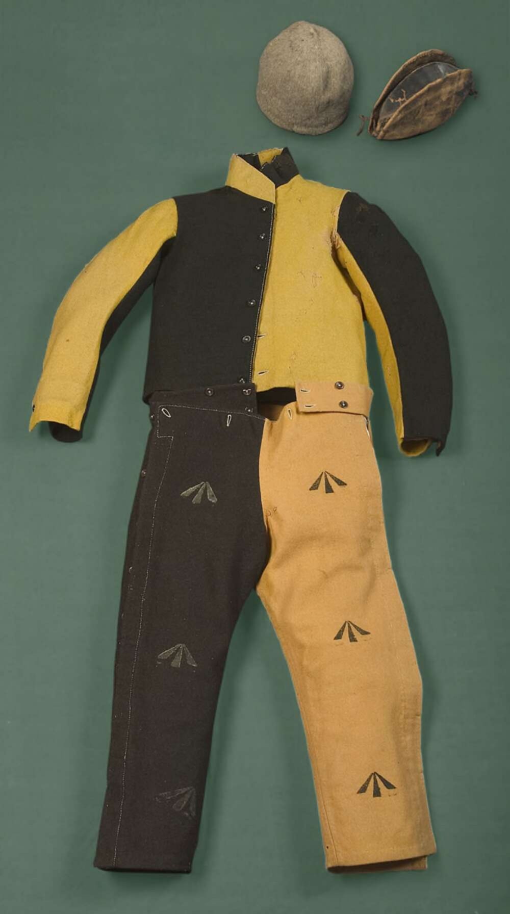 A woolen parti-colour jacket and trousers, with two leather caps. The trousers are stamped with broad arrow markings.