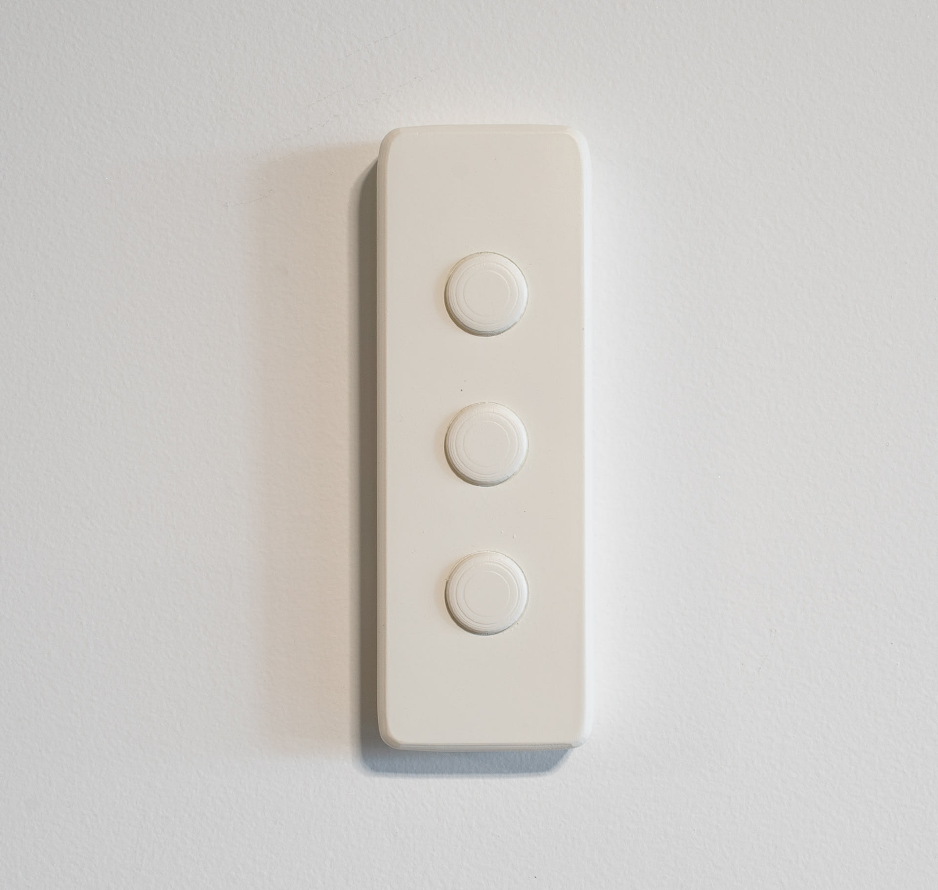 White wall-mounted sculpture, rectangular with three circular buttons in centre. 