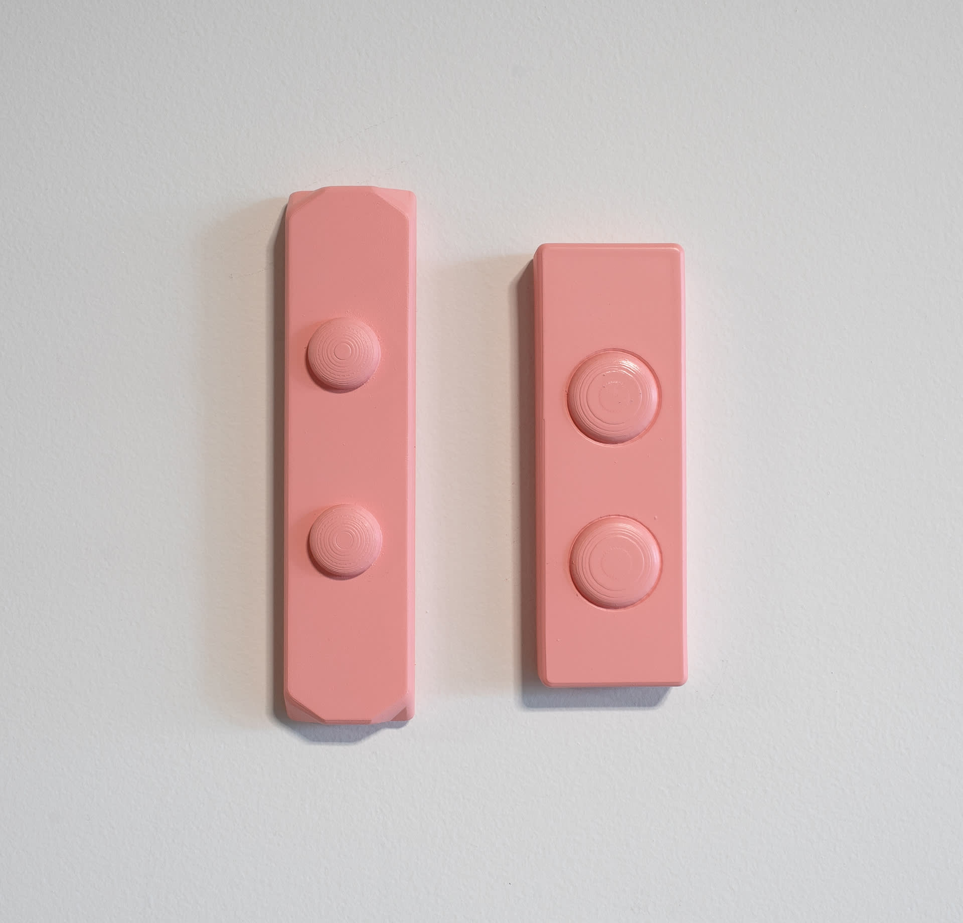 Two pink wall-mounted sculpture, rectangular with two circular buttons in centre.