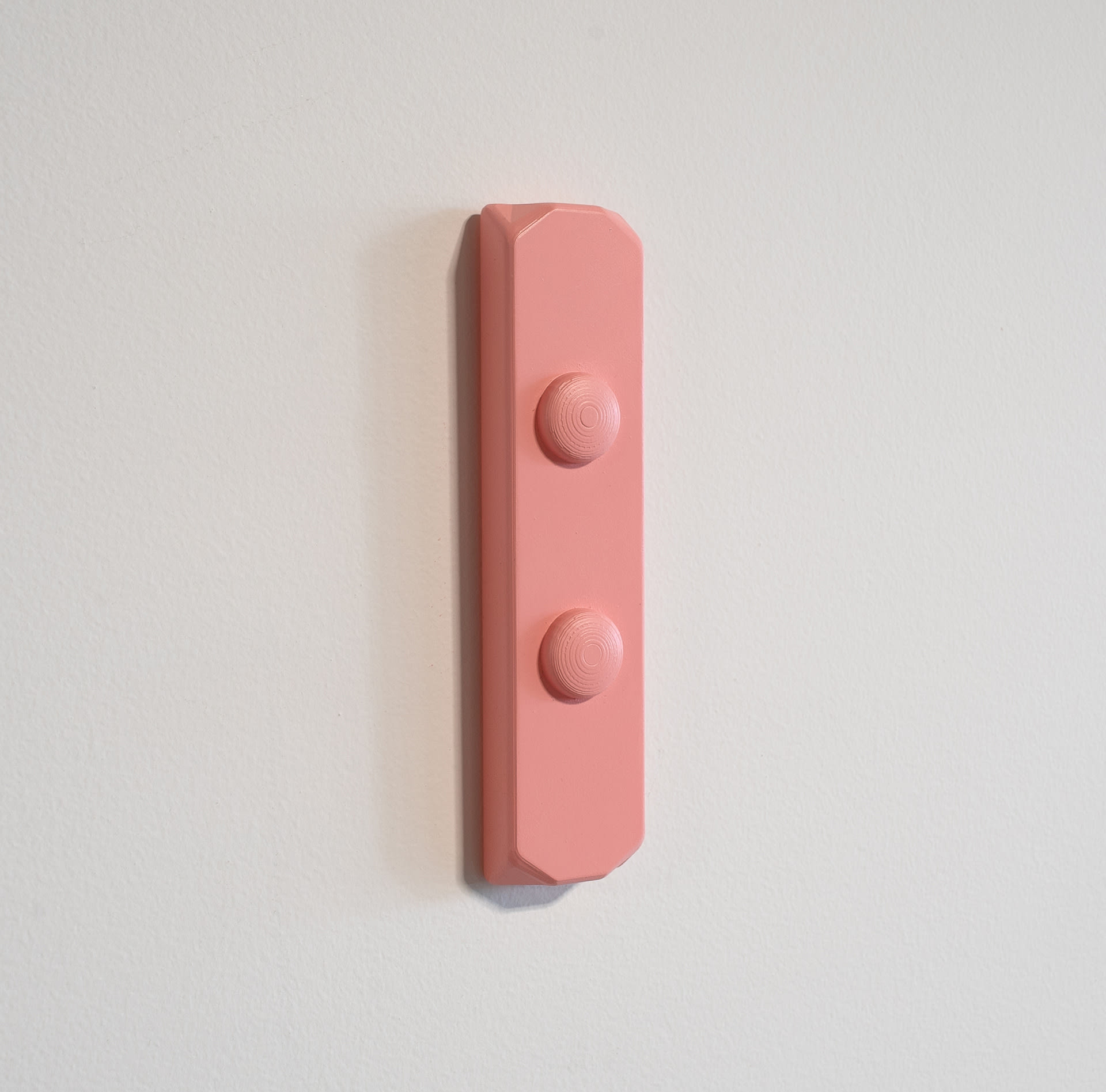 Pink wall-mounted sculpture, rectangular with two circular buttons in centre.