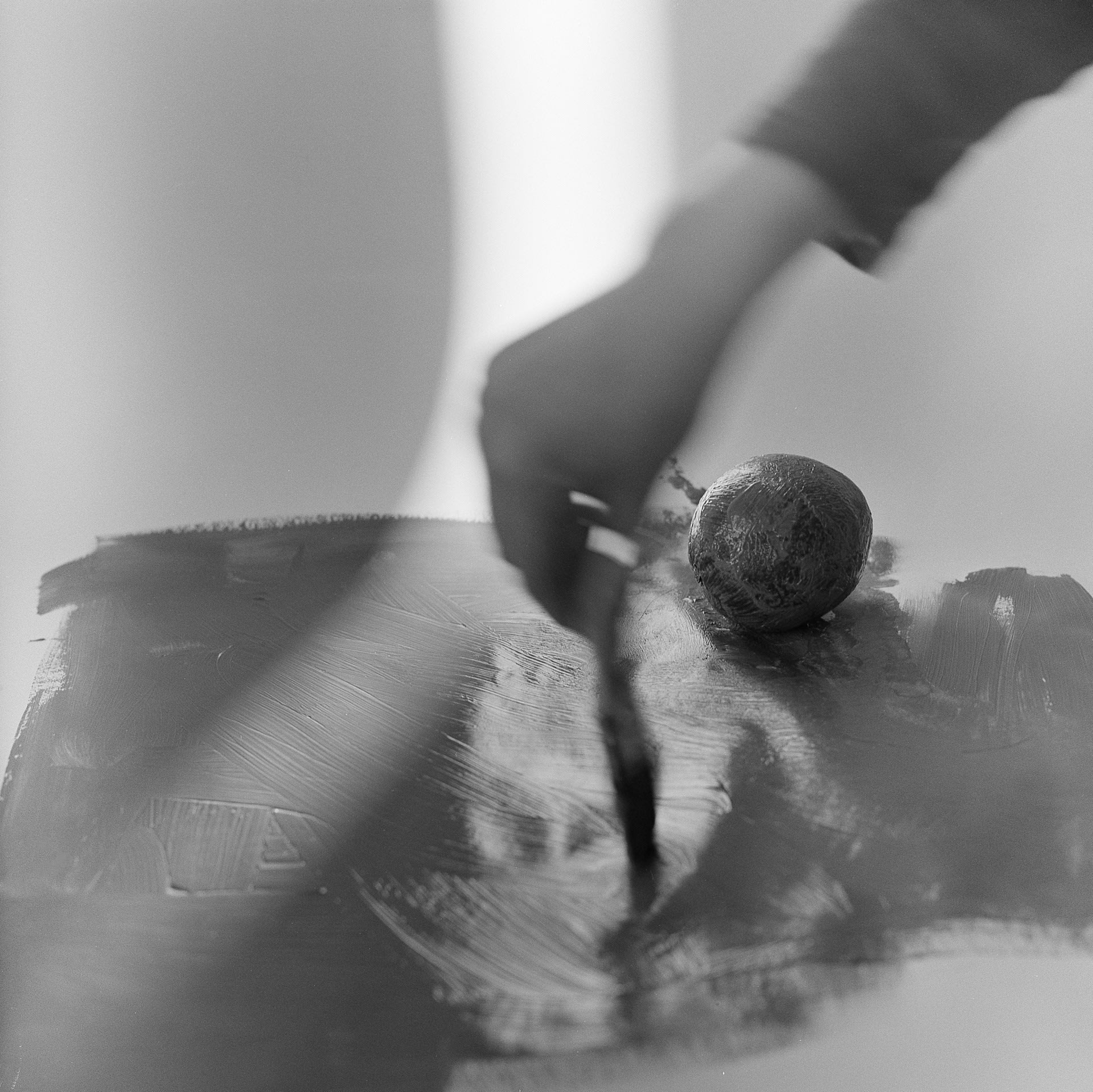 A hand in motion painting the floor, with a painted orange in the background and a strip of light to the right