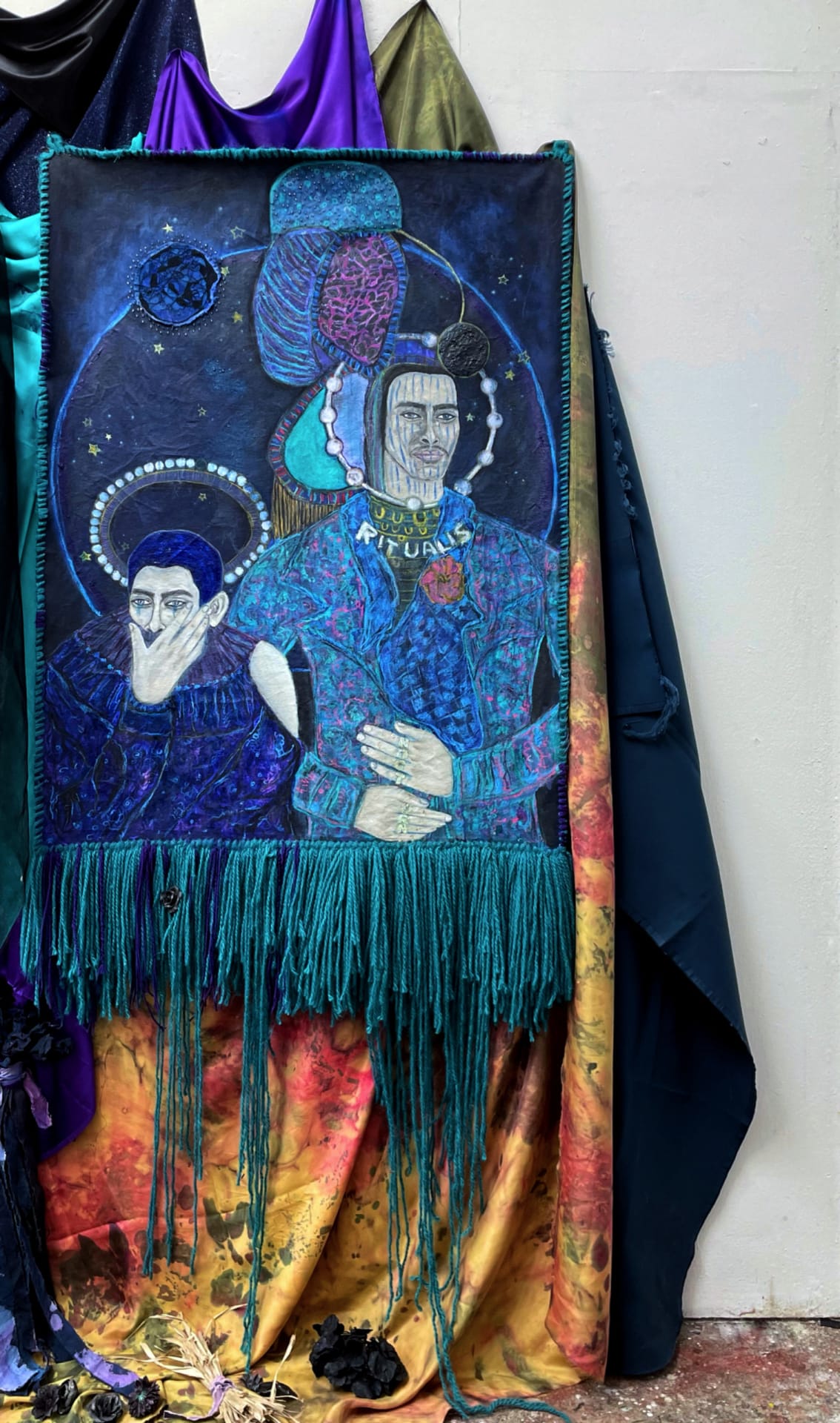 Two overdressed male figures on the blue black background with stars, with turquoise tassels 