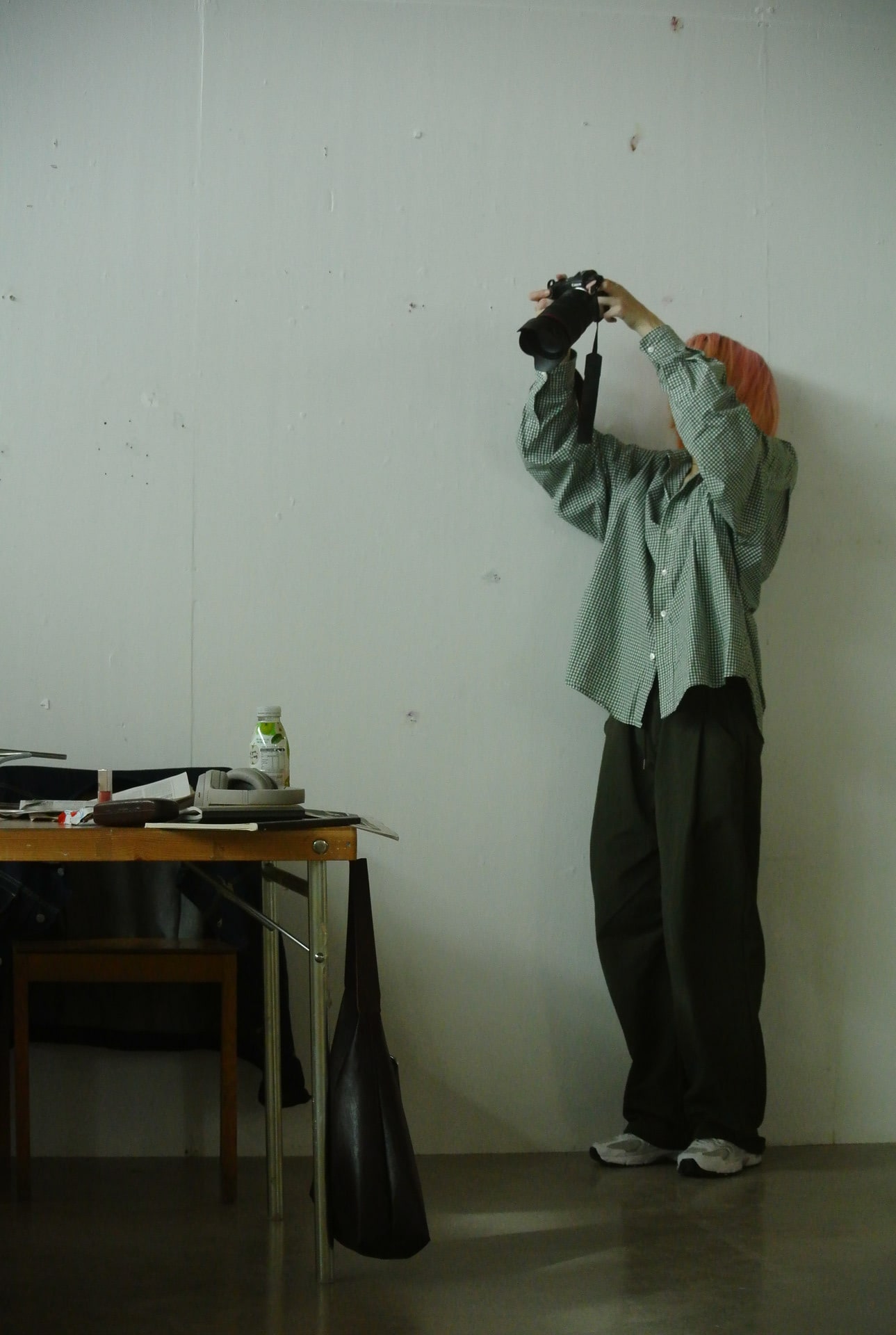 a person dressed in a green shirt and dark, loose pants takes a photo of a cluttered table.