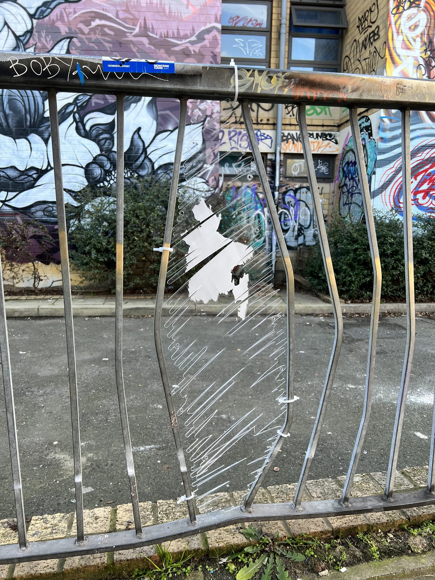 Gap in railings filled with a clear acrylic laser cut shape of a scribble to emulate graffiti. Object has image of Bangladesh 