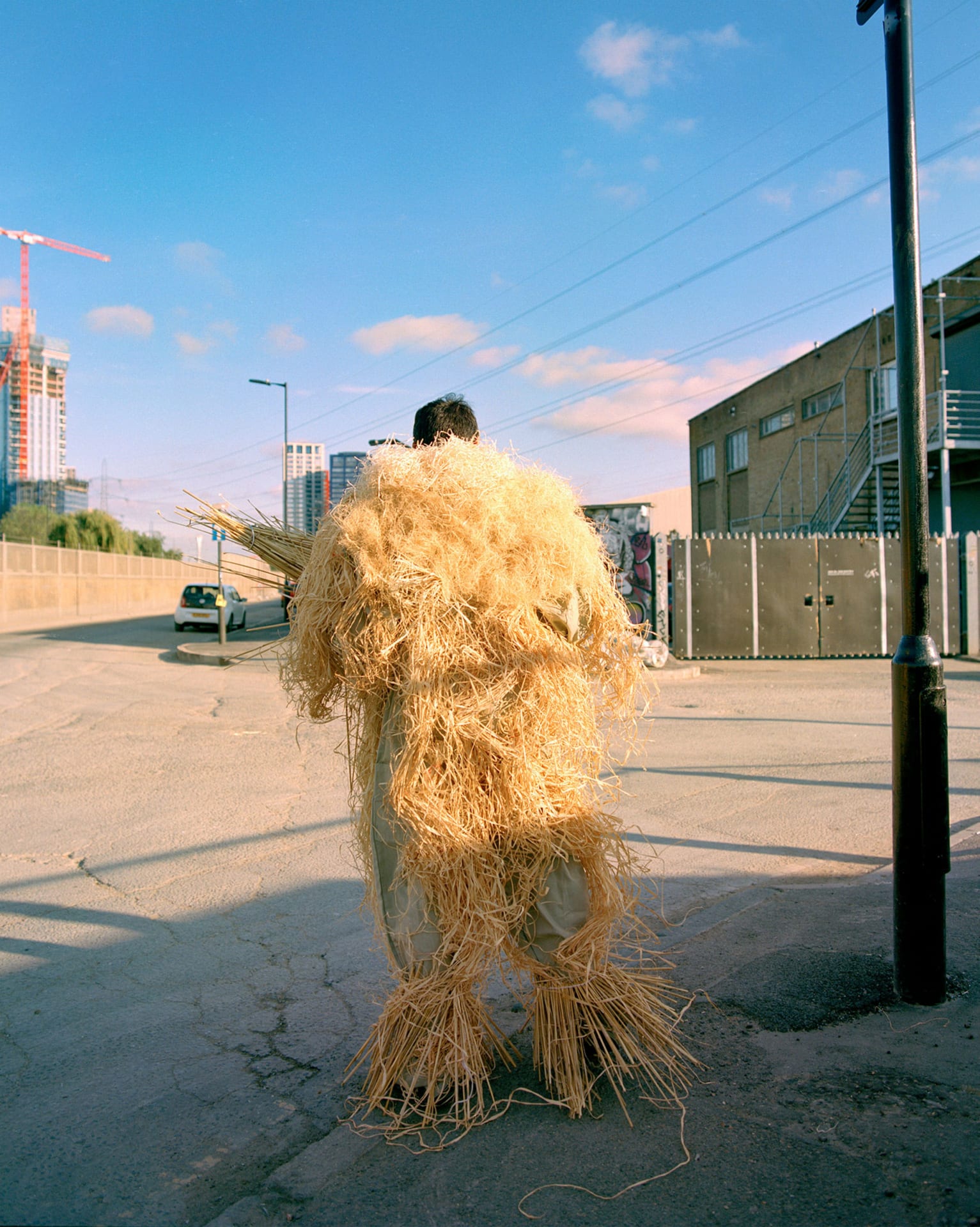 A lone figure of straw and masquerade standing in an urban landscape
