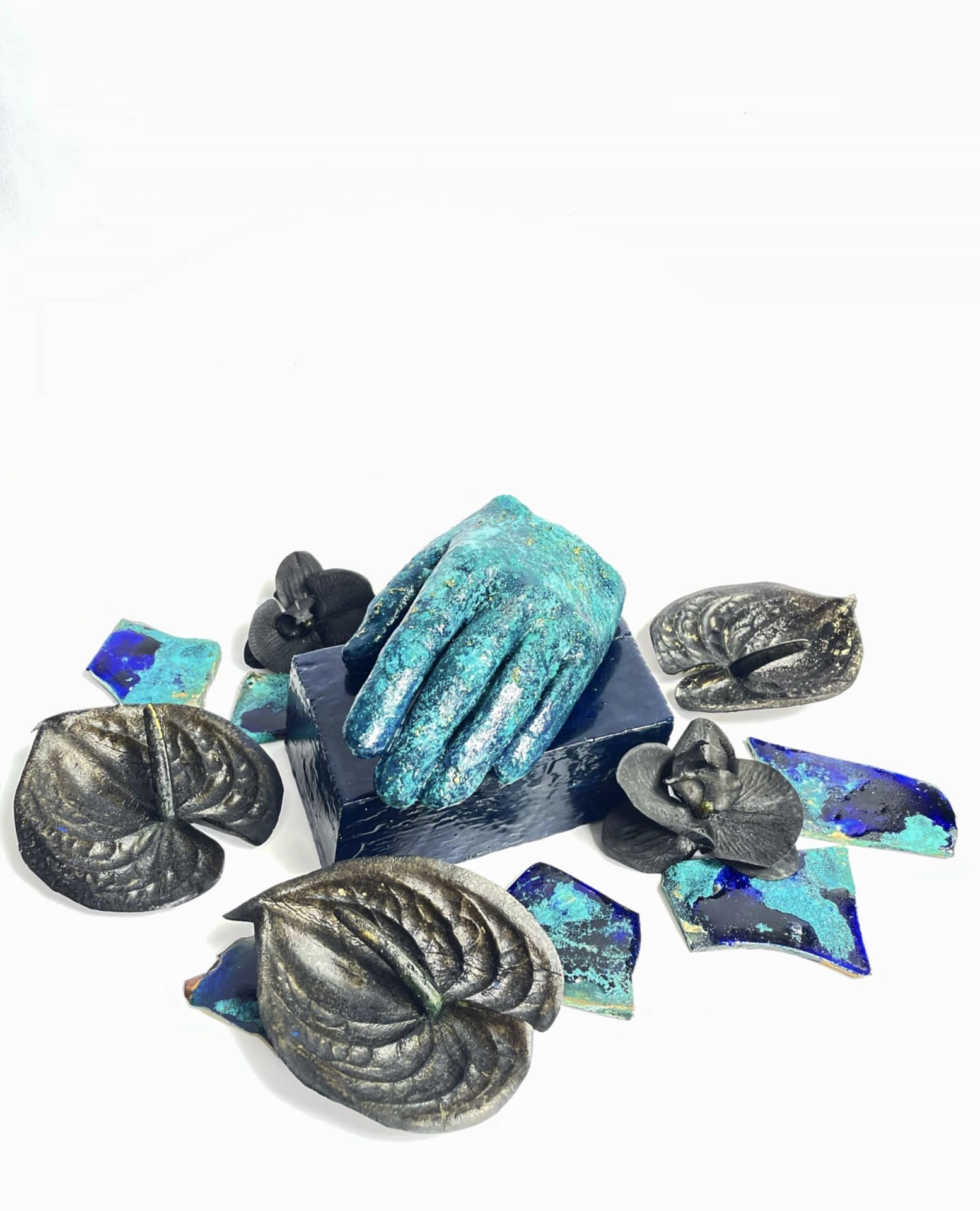 cast of a hand on a blue wooden base with artificial flowers around and clay pieces placed in front