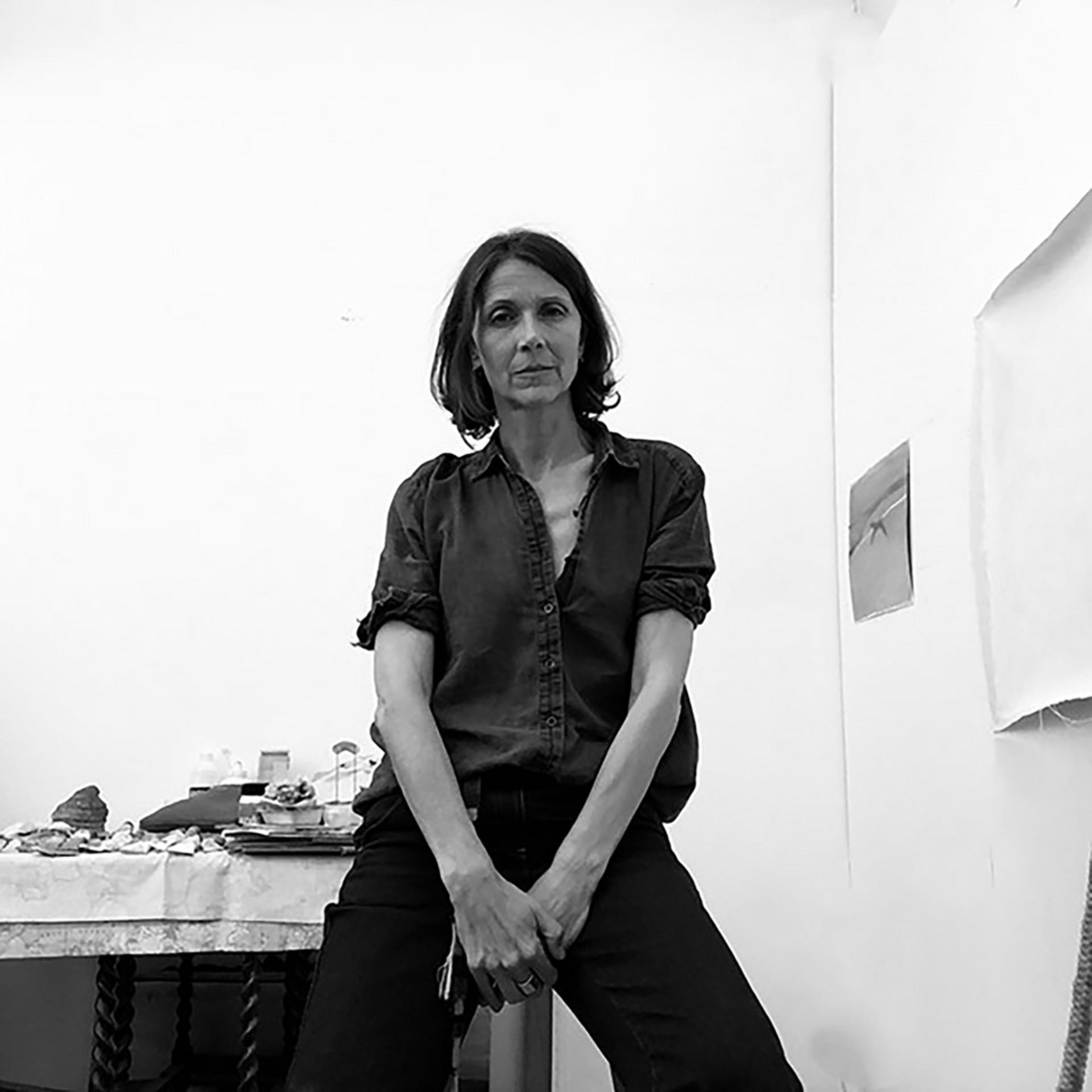 black and white image of a white woman, brown shoulder length hair, open shirt and dark jeans, looking directly at the camera   