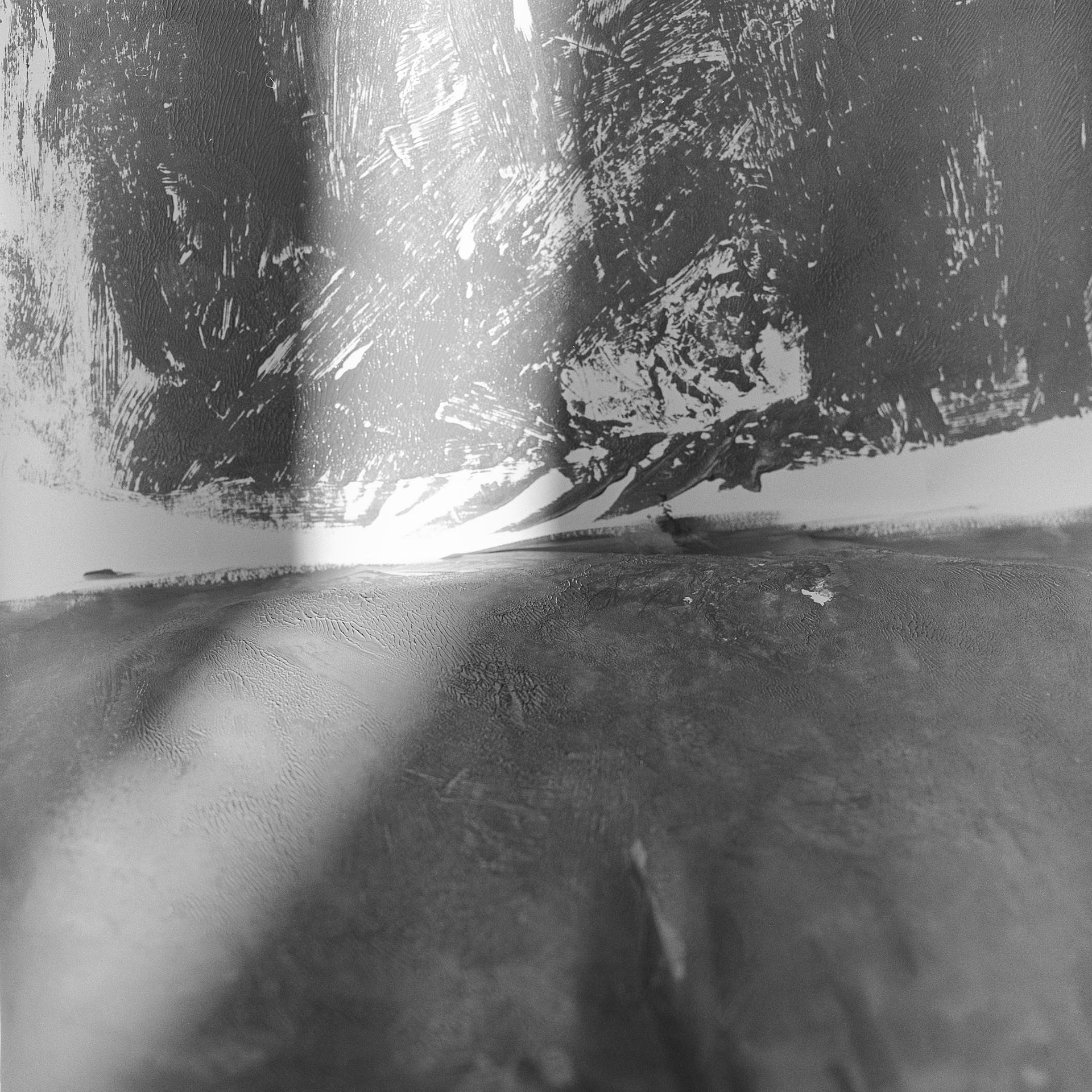 A black and white abstract image of a textured painted floor and wall with a streak of light off centre