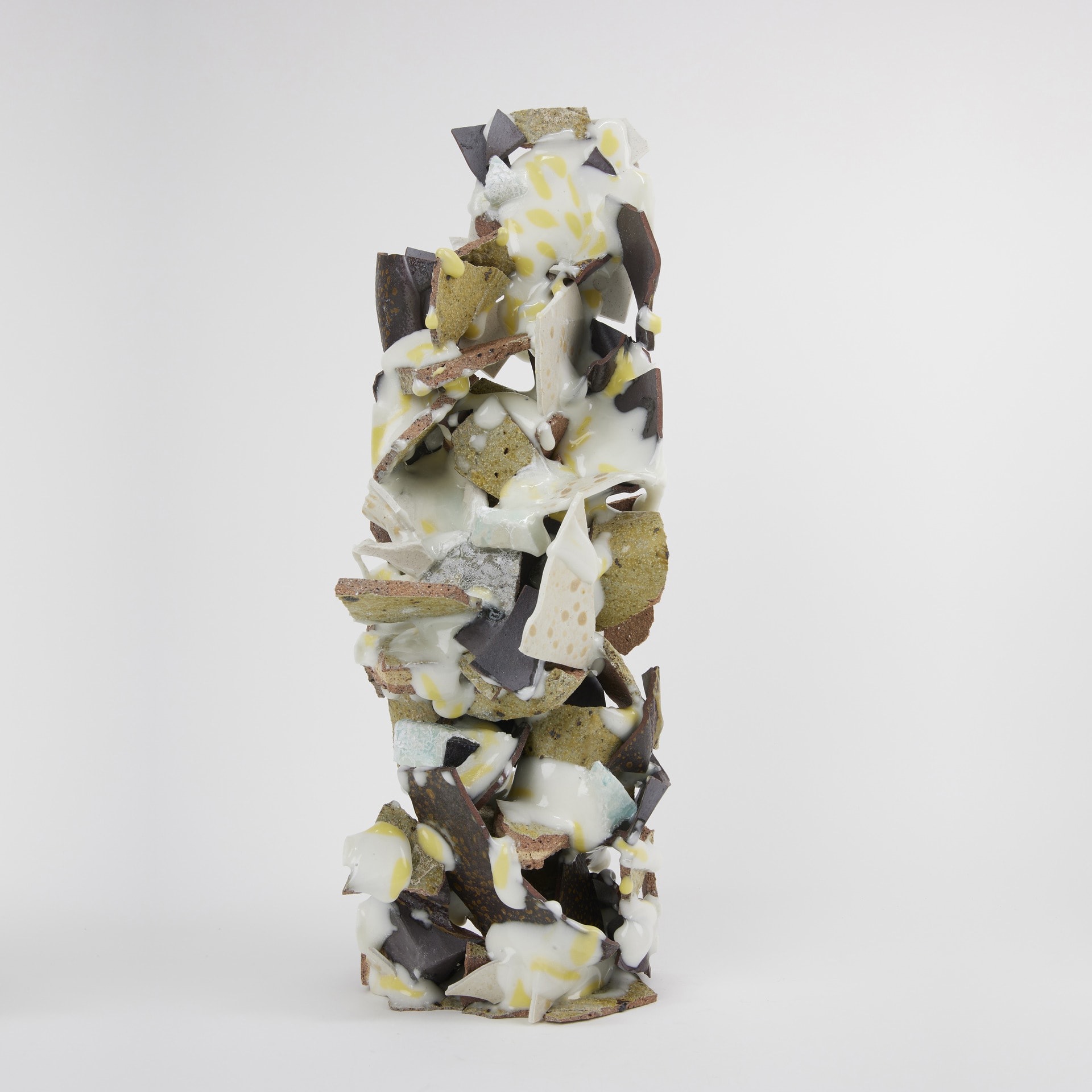 a pile of ceramic fragments (grey green, brown and white) fused into a tall column shape with globules of white and yellow glaze