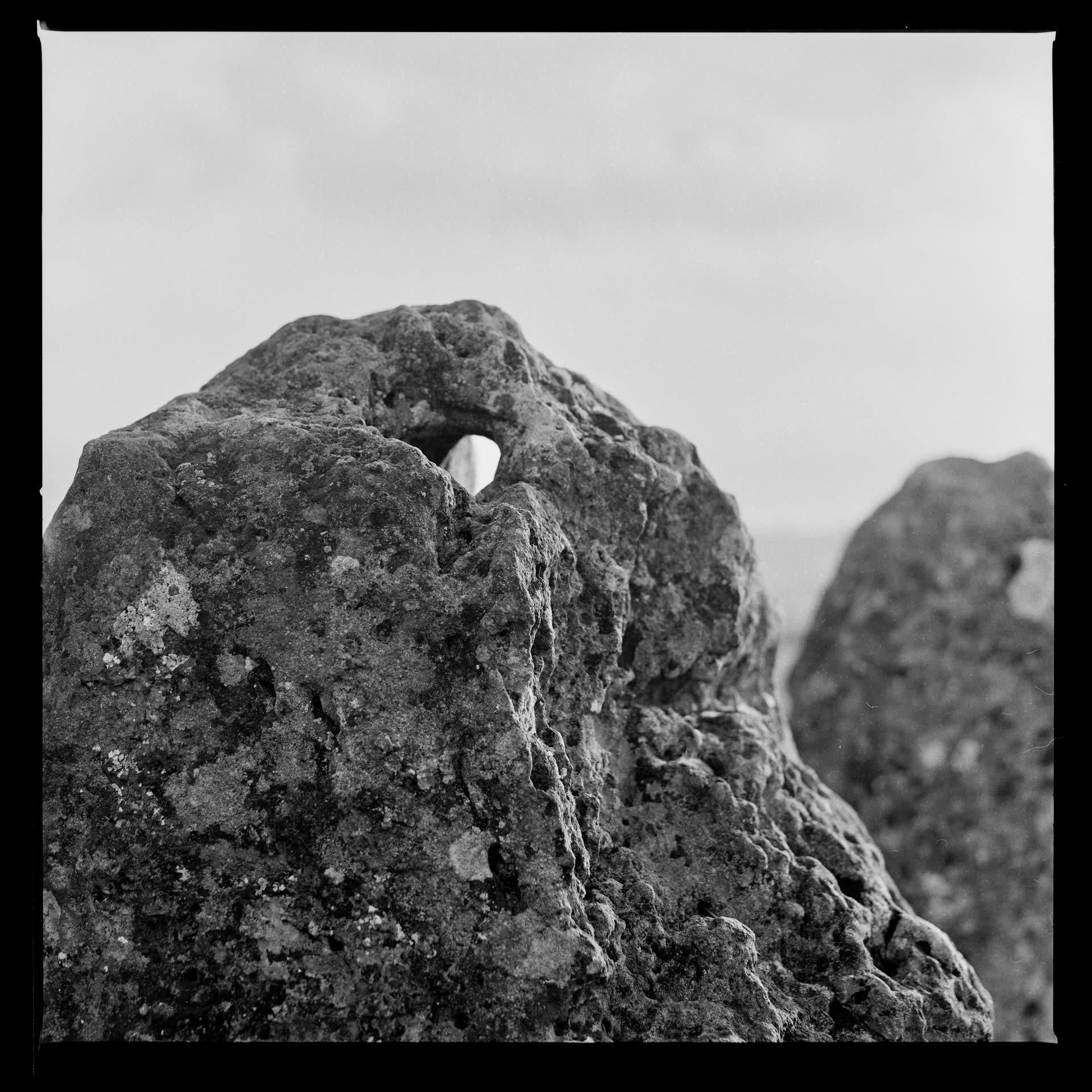 a single standing stone with a hole through the top showing the sky on the other side. Black and white photograph.