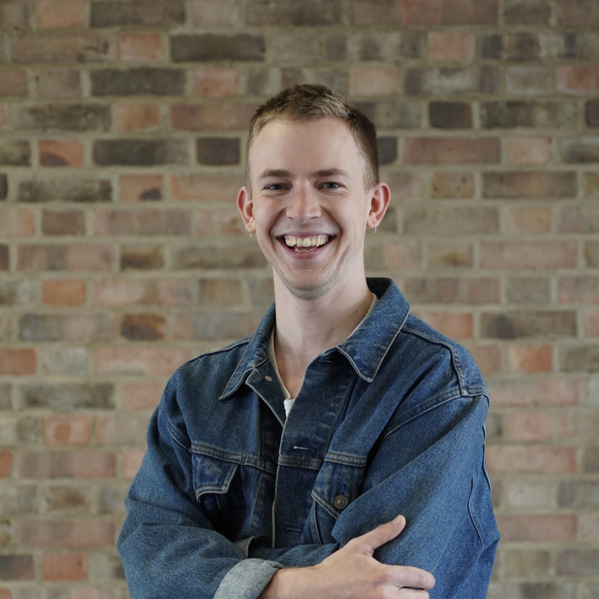 blonde man in denim jacket in front of brick wall