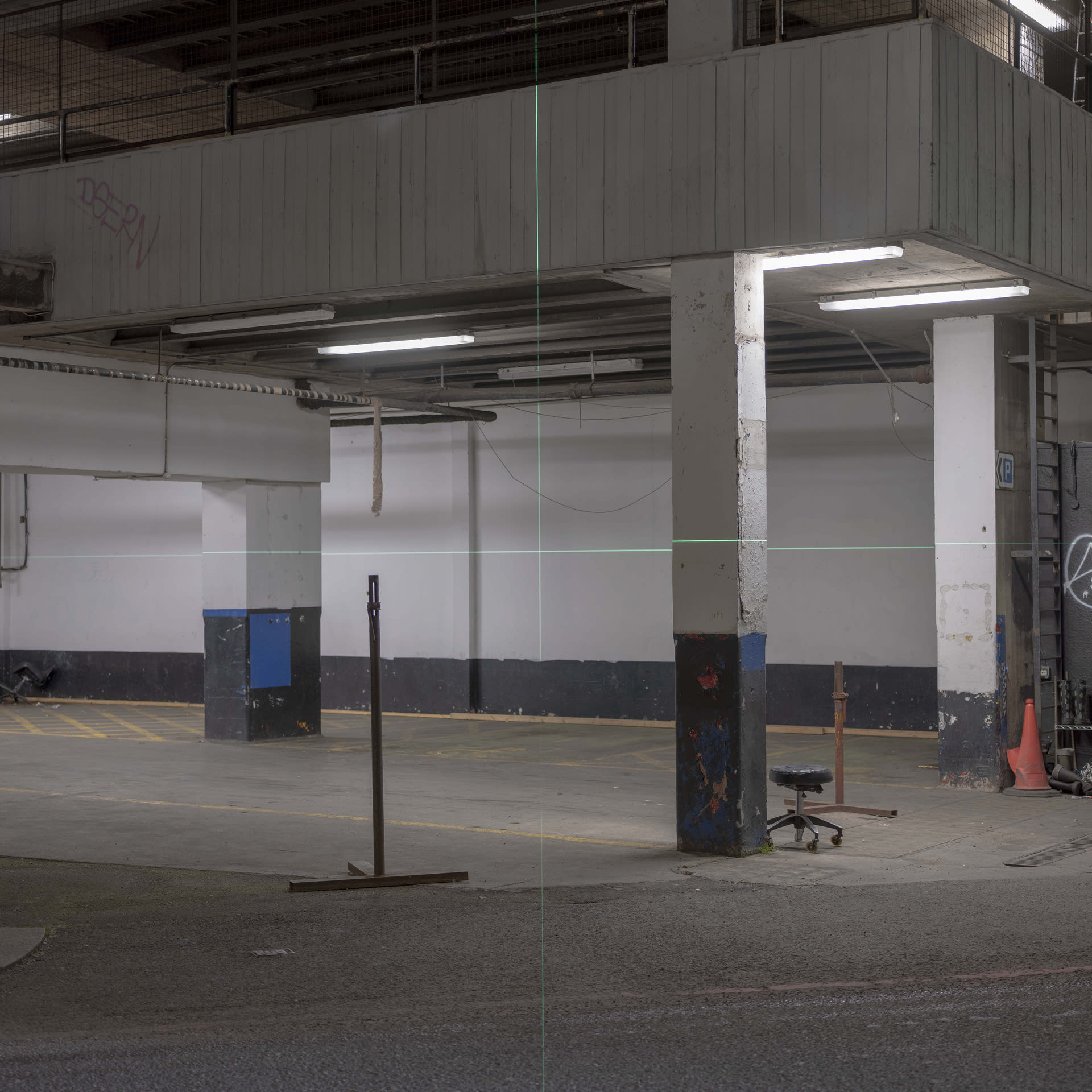 A green cross-shaped laser is projected on car park