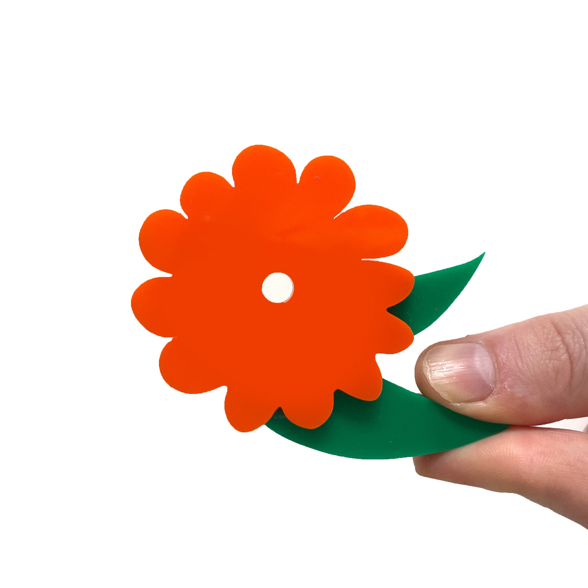 Flower plastic model held between two fingers on a white background. The petals are burnt orange with green leaves.