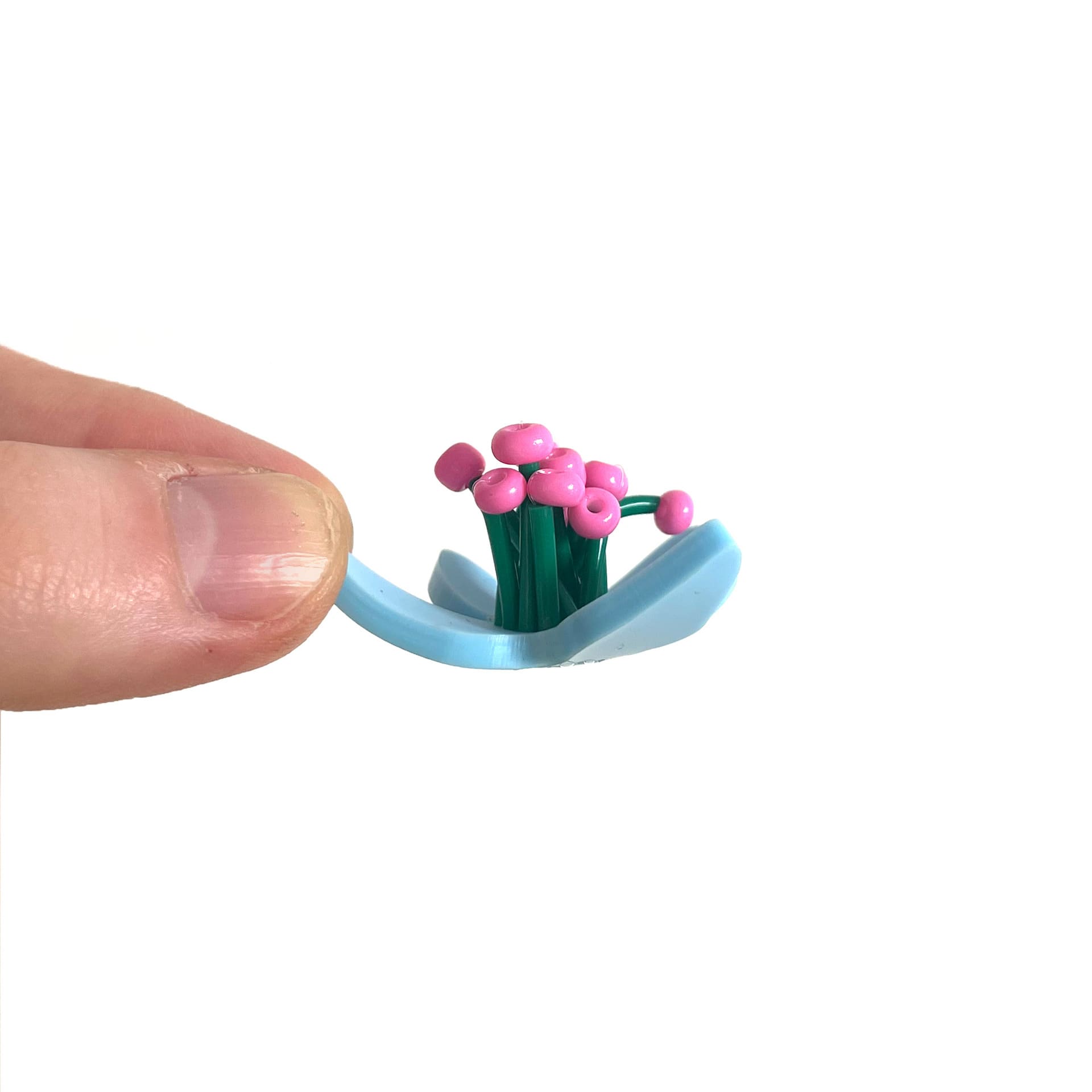 Flower plastic model held between two fingers on a white background. The petals are baby blue with added green embellishment.