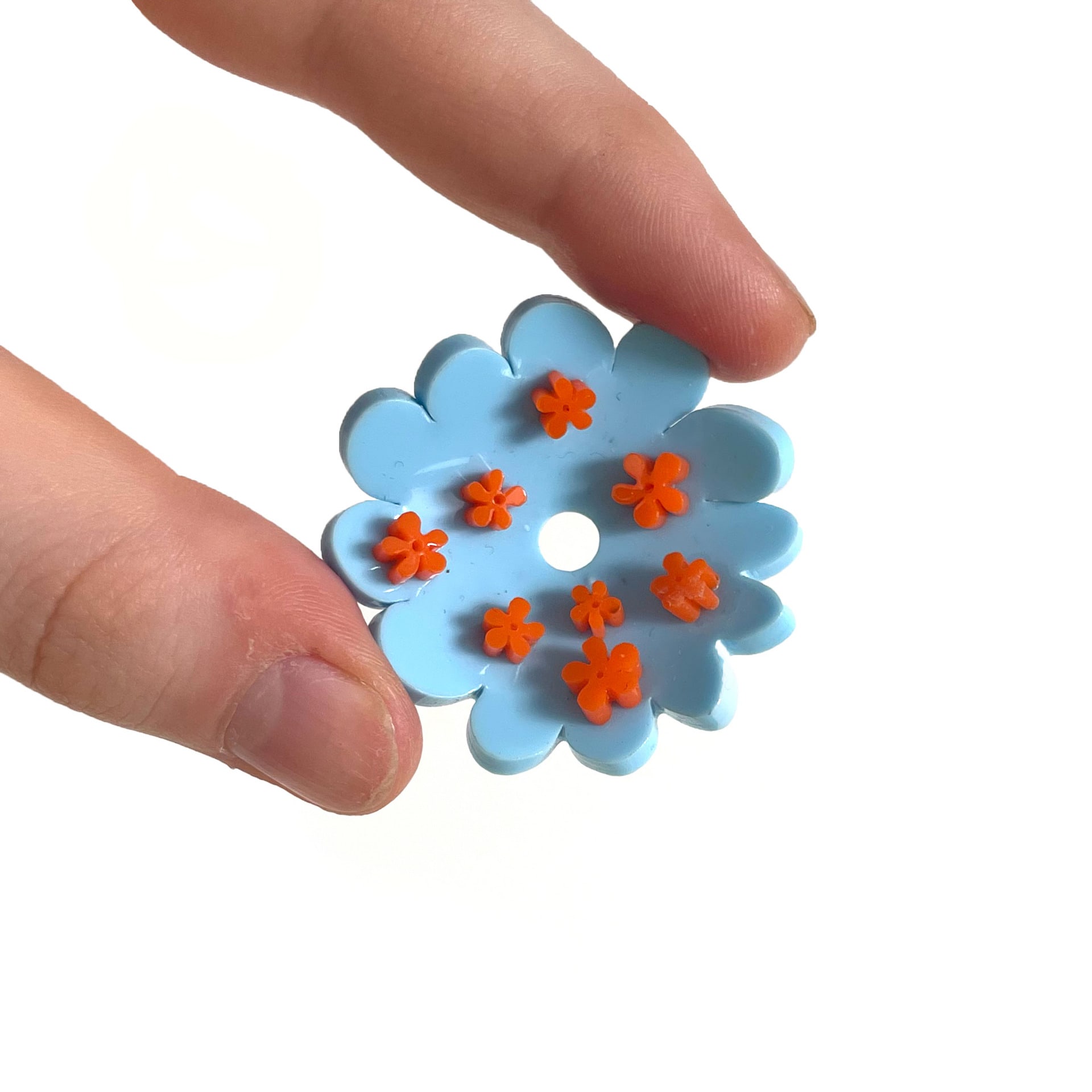 Flower plastic model held between two fingers on a white background. The petals are baby blue with orange details..