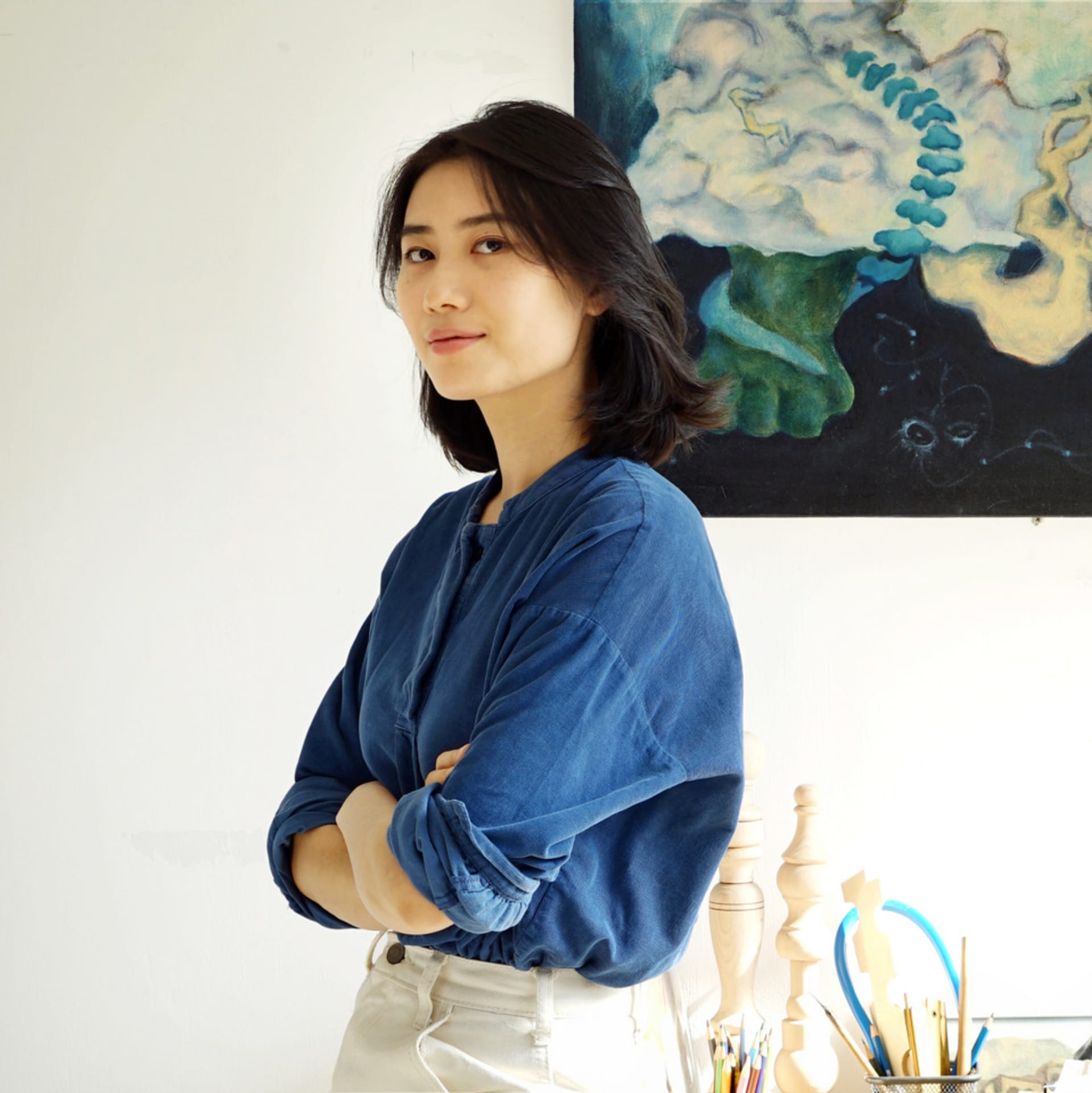 A photo of an artist wearing a blue shirt, standing with crossed arms.