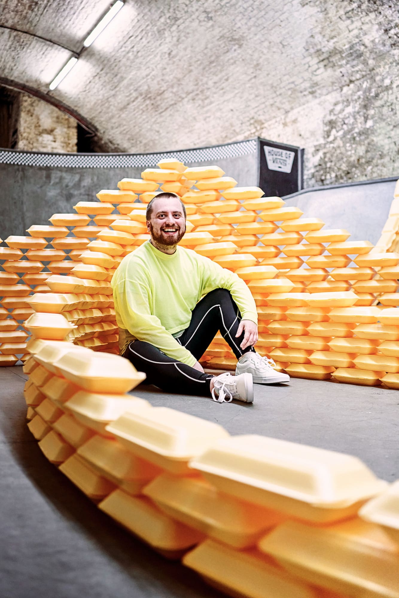 Jacob is sat amongst take away containers at the bottom of a skate boarding bowl. The boxes are stacked like waves crashing.