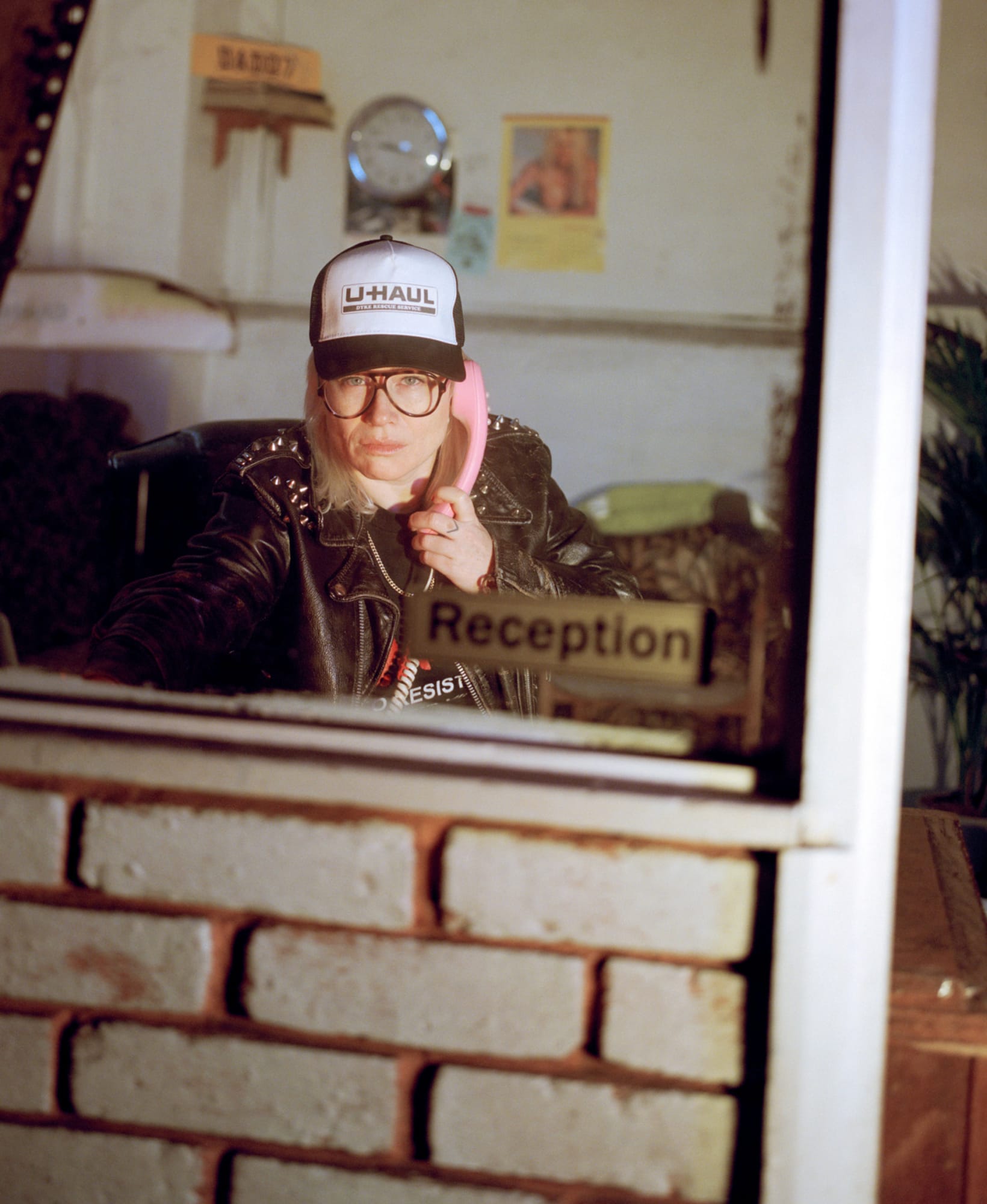 A photograph of the U-Haul Dyke Rescue Service hotline operator in a reception booth, answering a pink telephone 