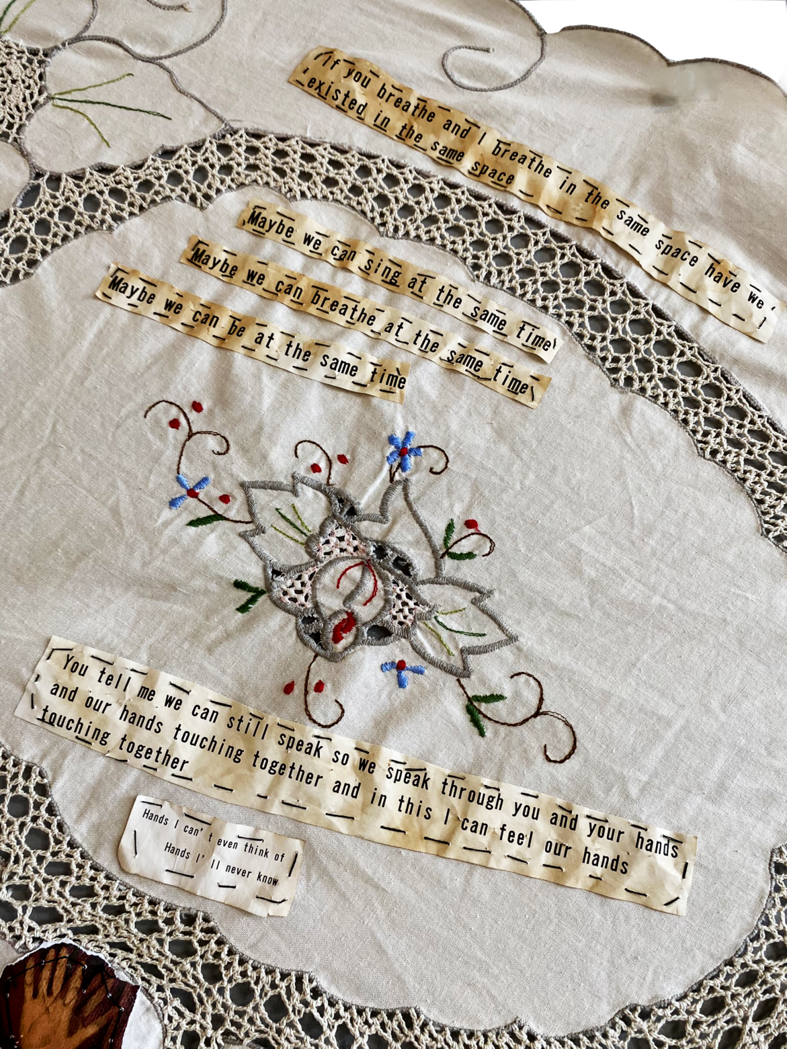 Detail of embroidered tablecloth with paper text stitched on (text not fully readable)