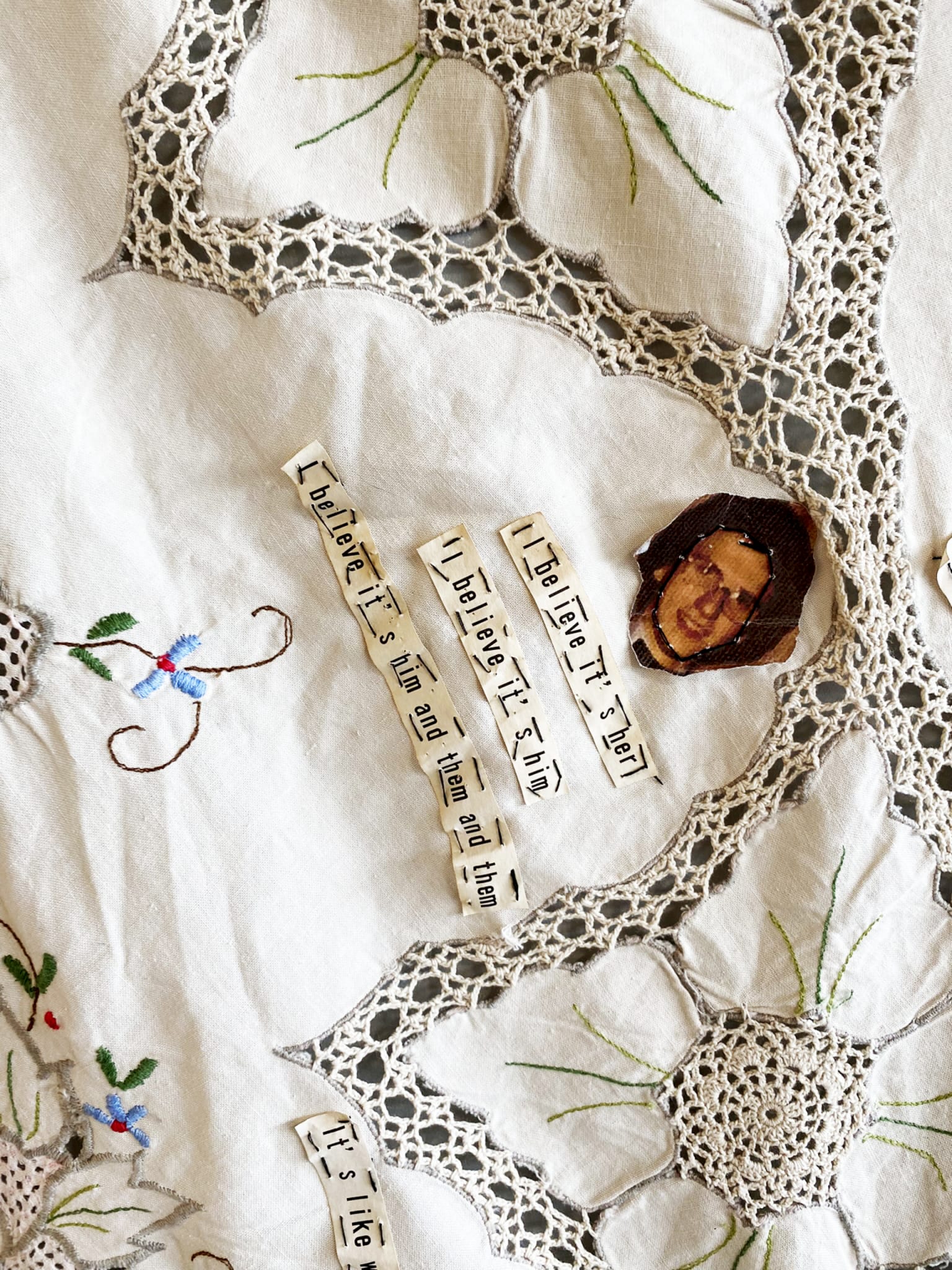 Detail of embroidered tablecloth with paper text stitched on (text not fully readable)