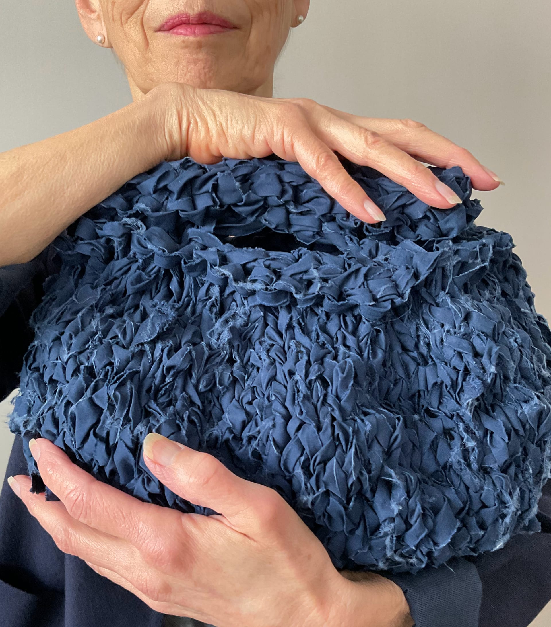 Round blue knitted fabric bag cradled by someone with pink lipstick