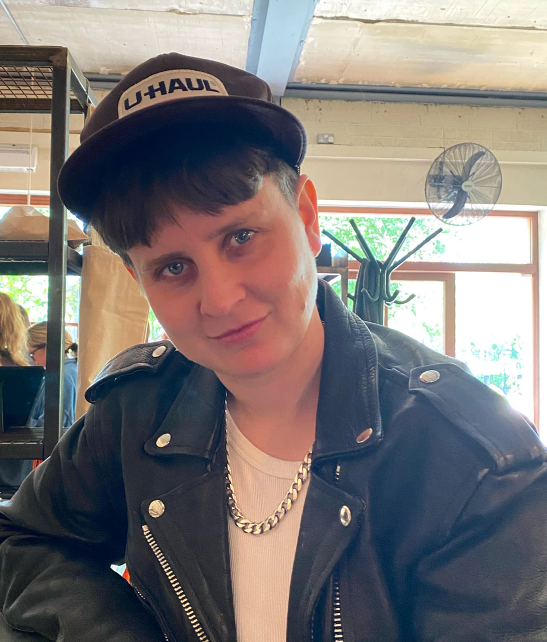 A photograph of Lucy Nurnberg, wearing a U-Haul cap and a leather jacket