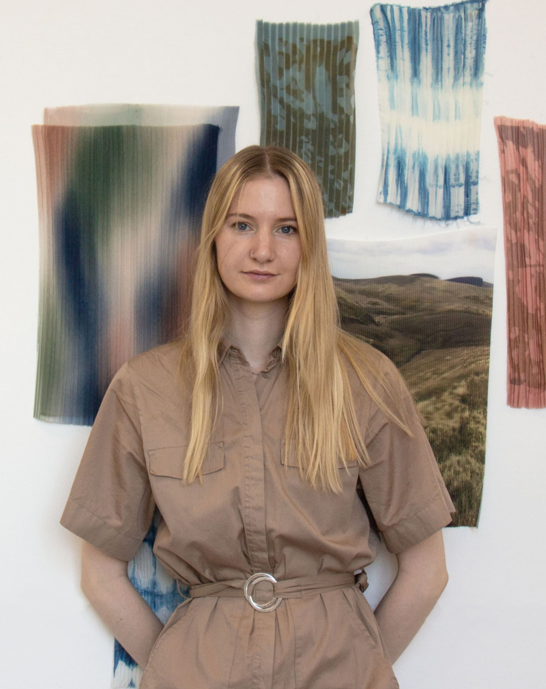 Linnéa standing in front of a wall of pleated colourful samples looking at the camera