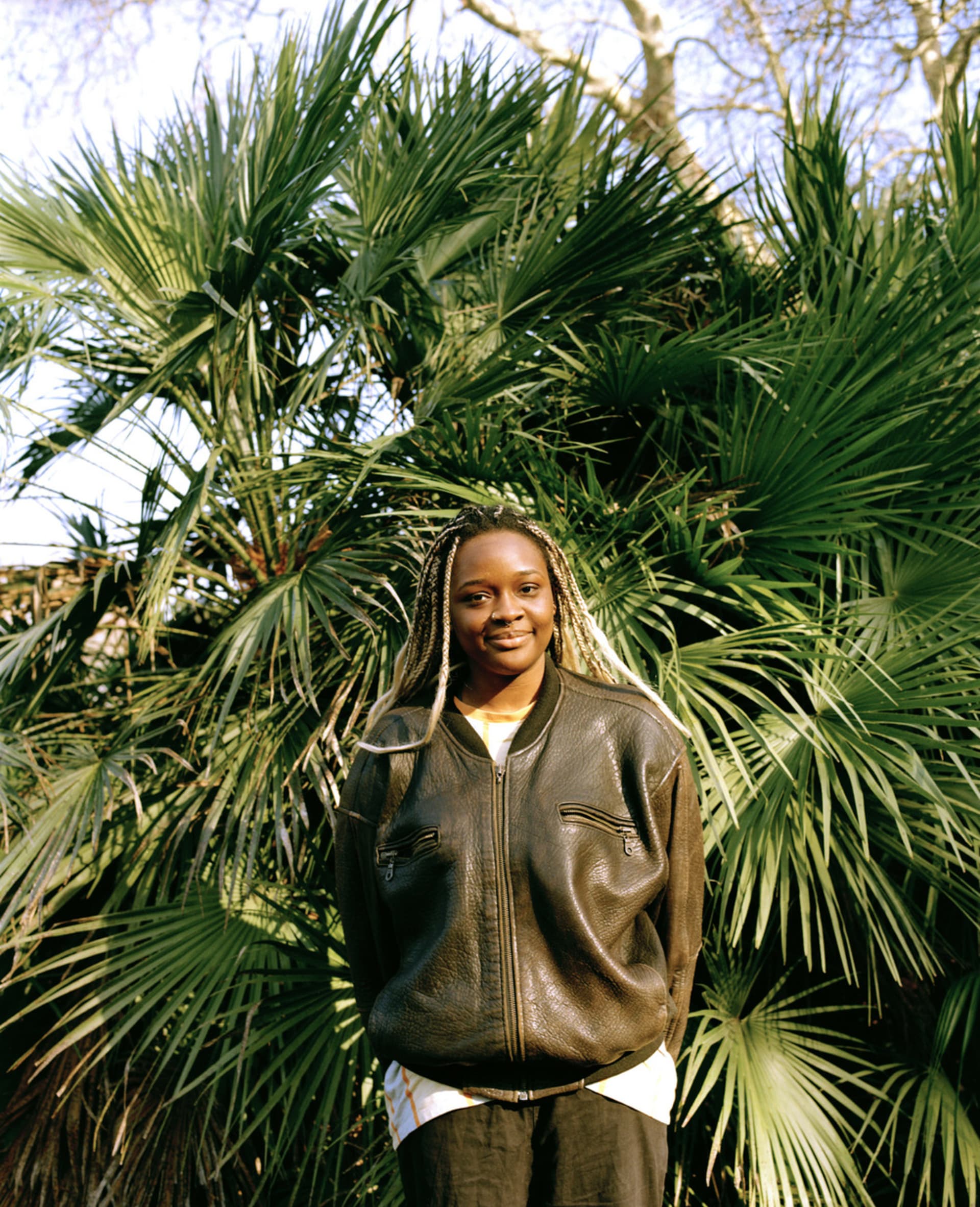 Photograph of Aisha Seriki standing behind a big plant in a garden