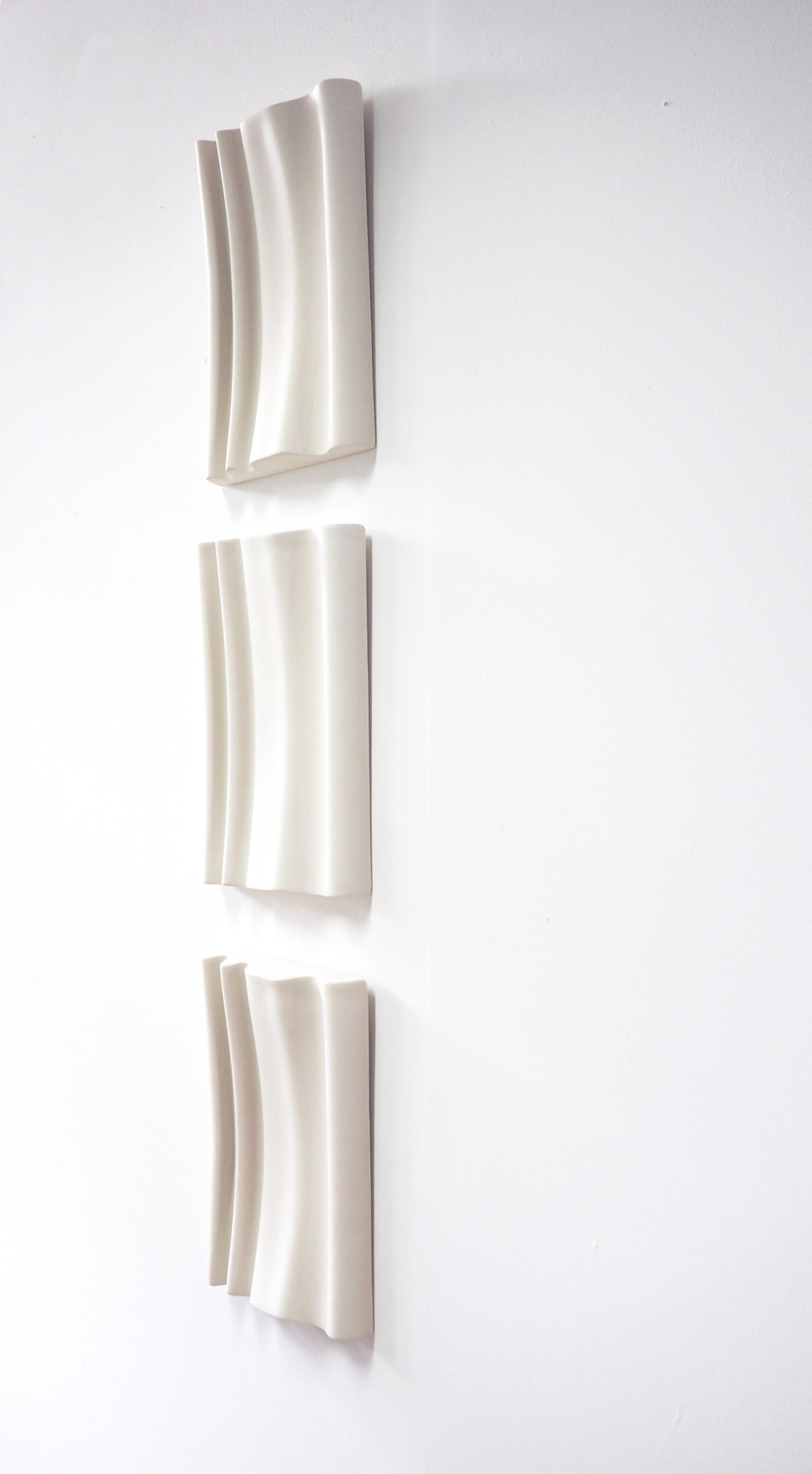3 undulating forms hung on a wall in a vertical line. they mimic the wave of curtains