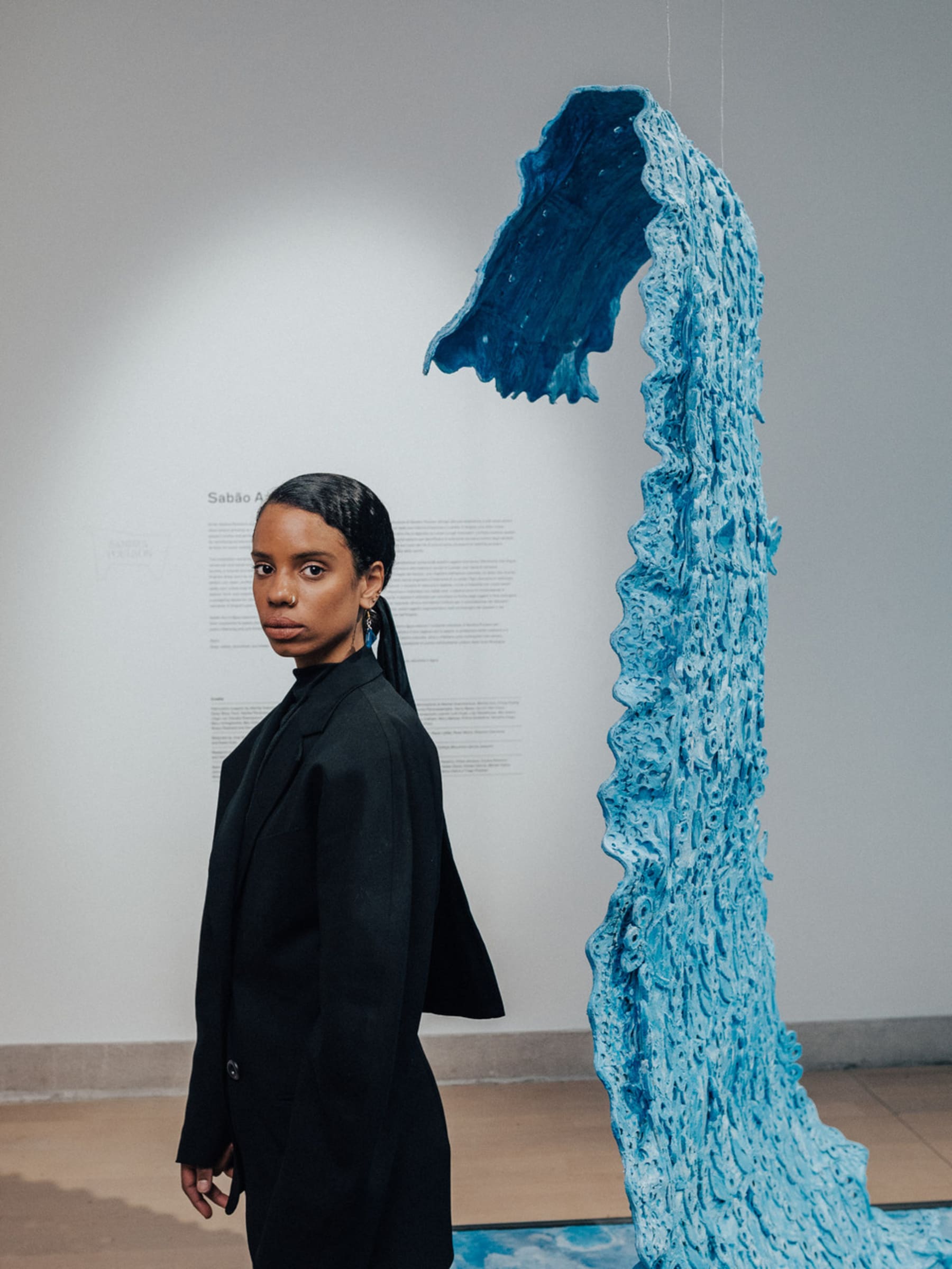 Sandra wears a black suit and  poses next to blue soap sculpture. 