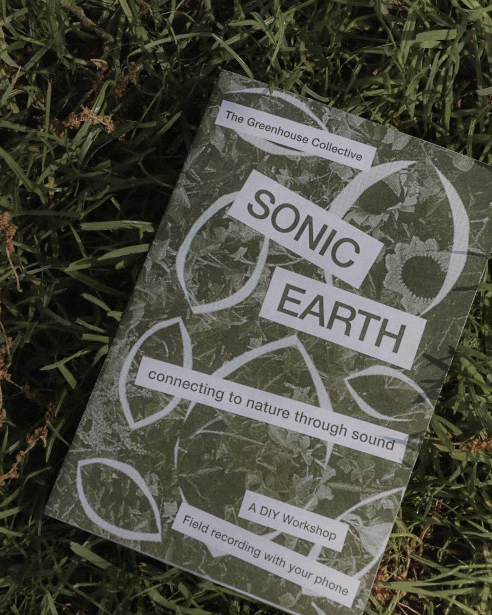 A photograph of a printed zine in some grass showing the front cover, including the title "Sonic Earth" and a collage background