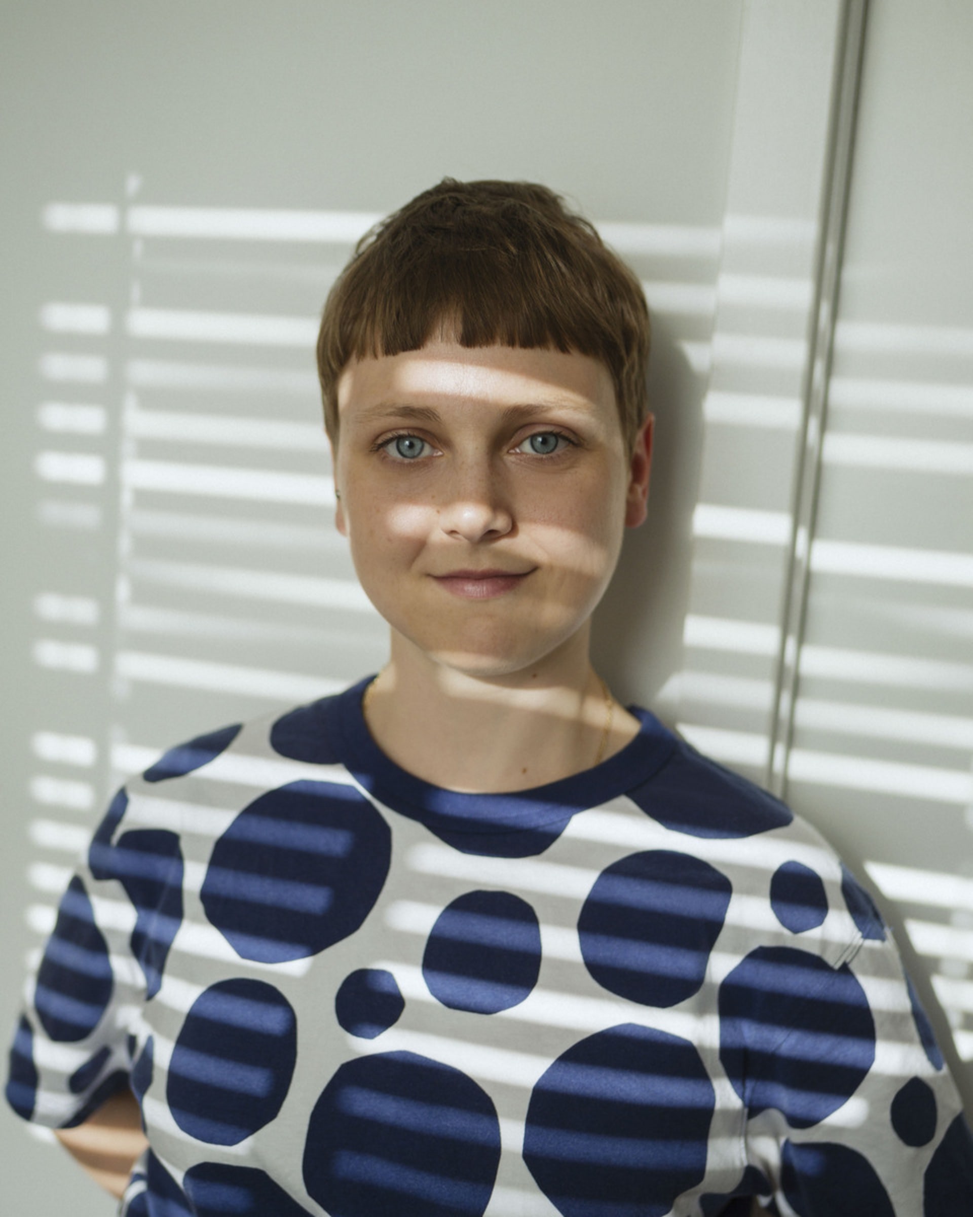 Nicci is a white person with short hair, shown smiling in blue and white polka dot t shirt.