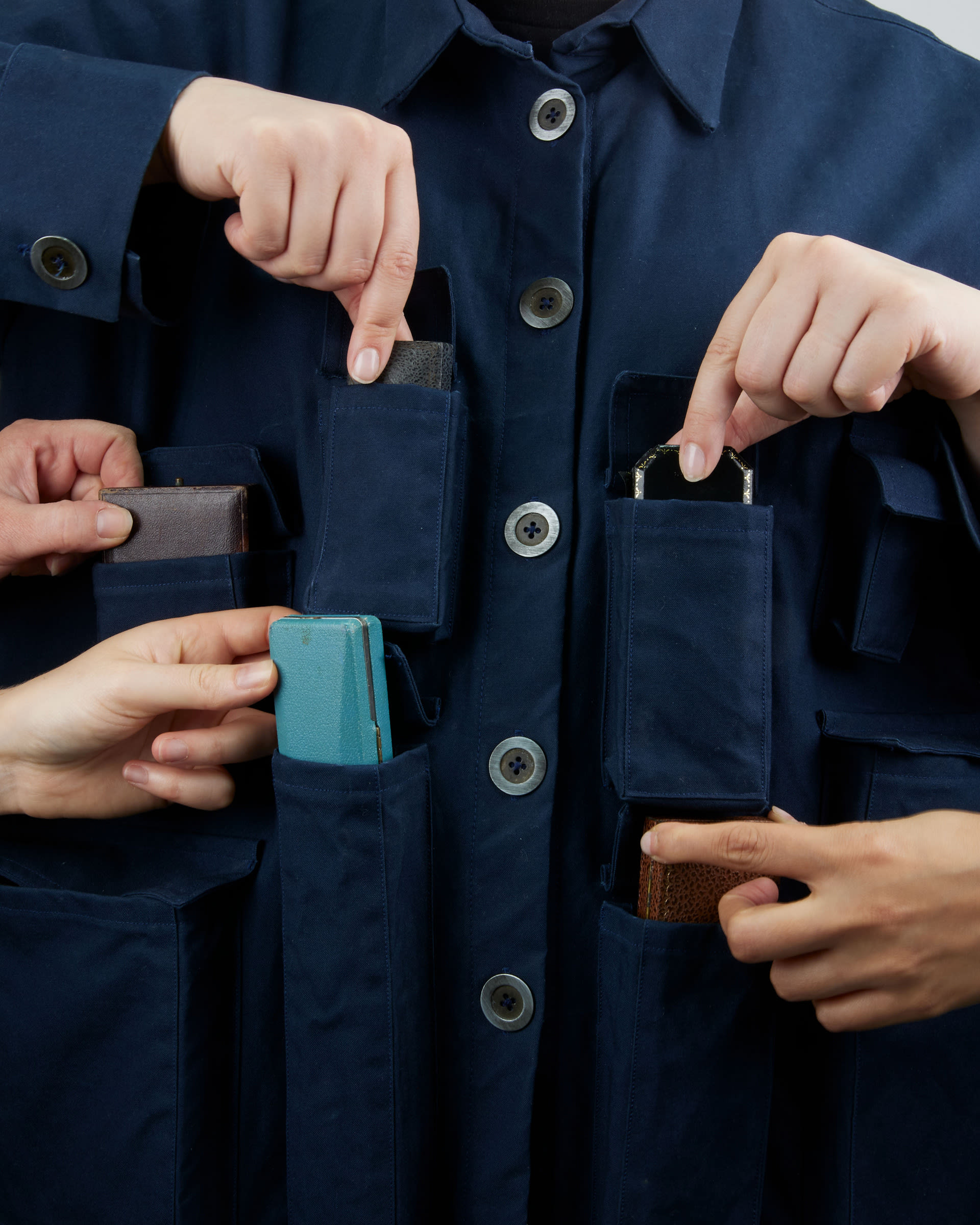 person wearing a jacket with lots of pockets full of vintage boxes, multiple hands reach in to frame to open the pockets